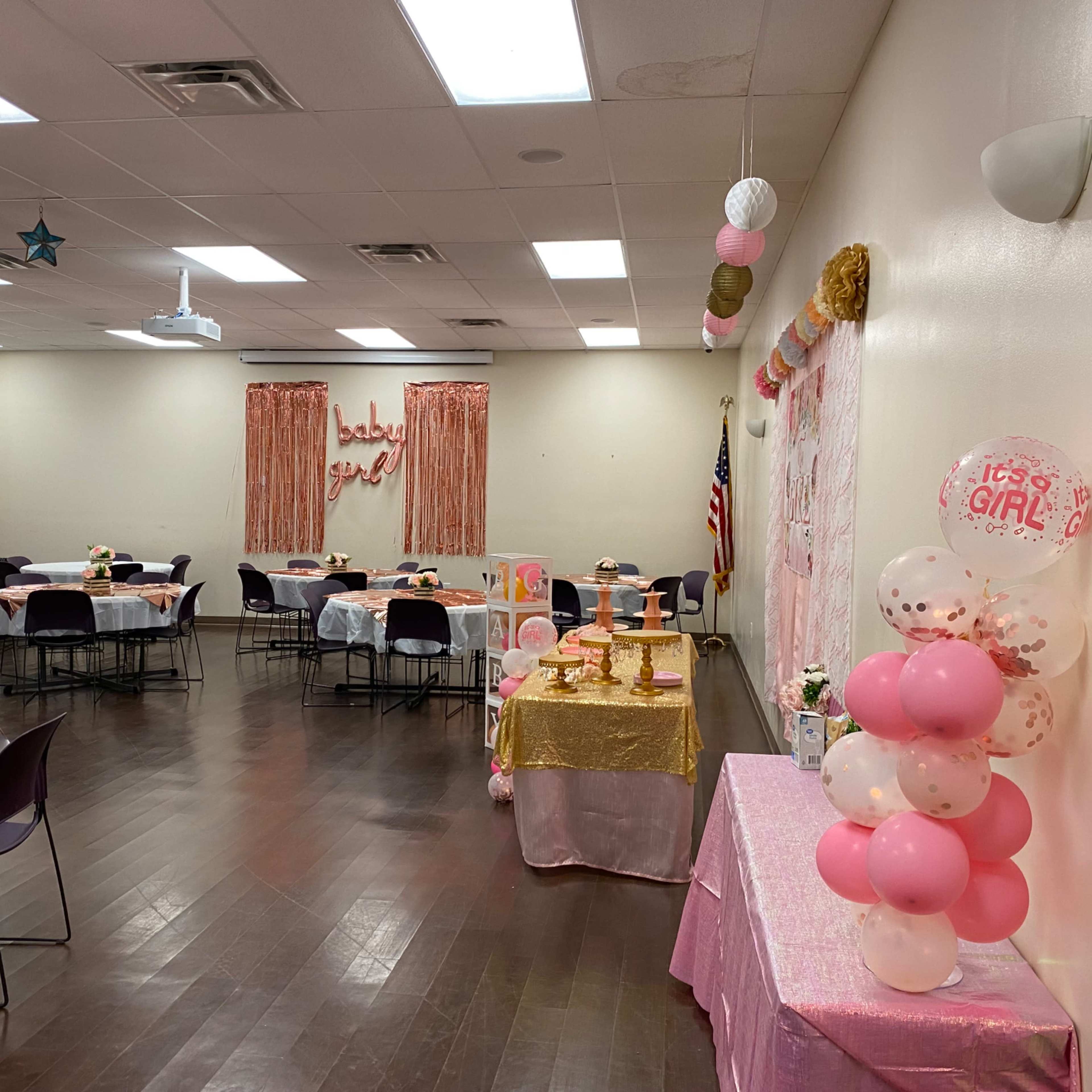 A decorated room for a baby shower with pink-themed tables, banners, and balloons.