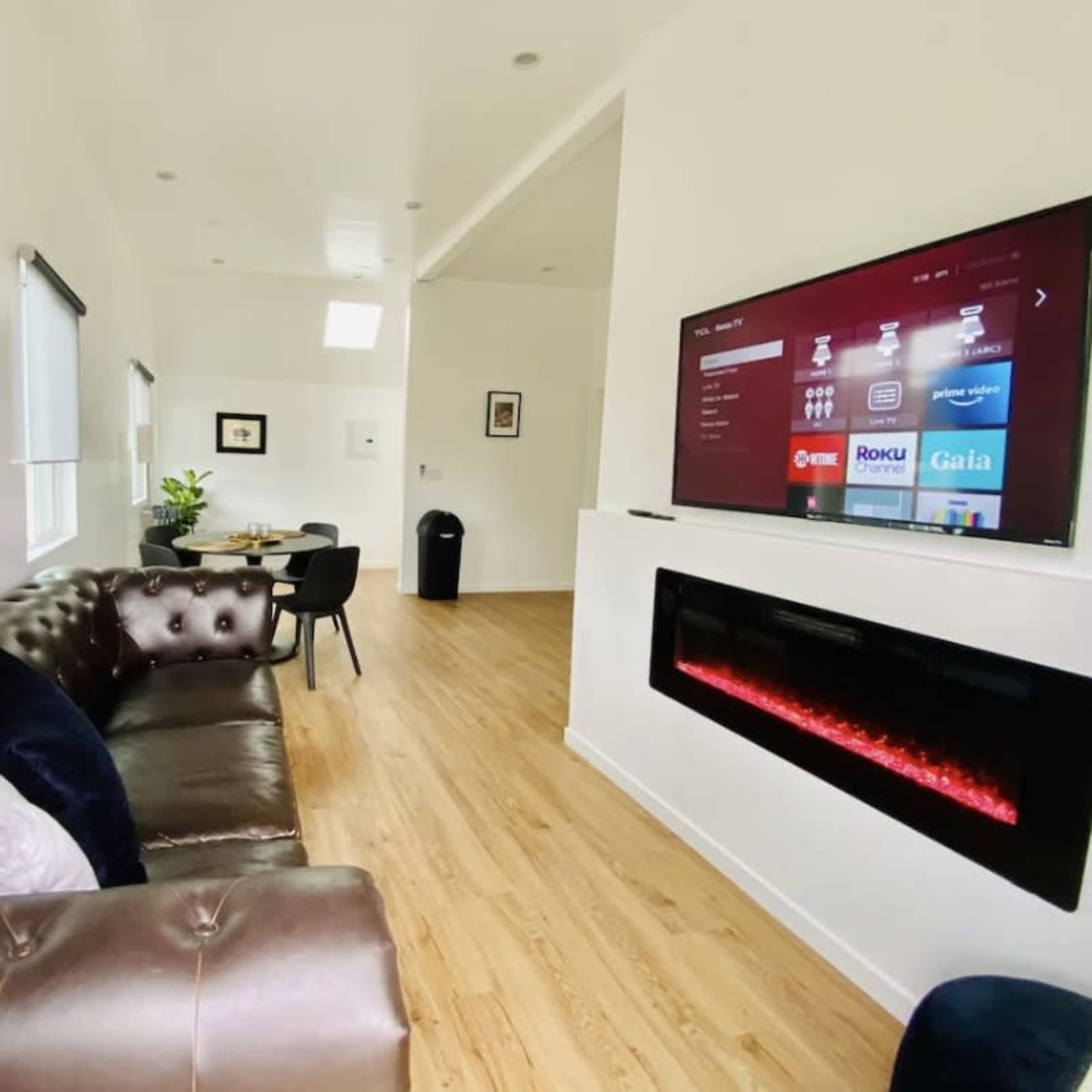 A modern living room featuring a dark leather sofa, a wall-mounted television displaying a menu, and an electric fireplace beneath it.