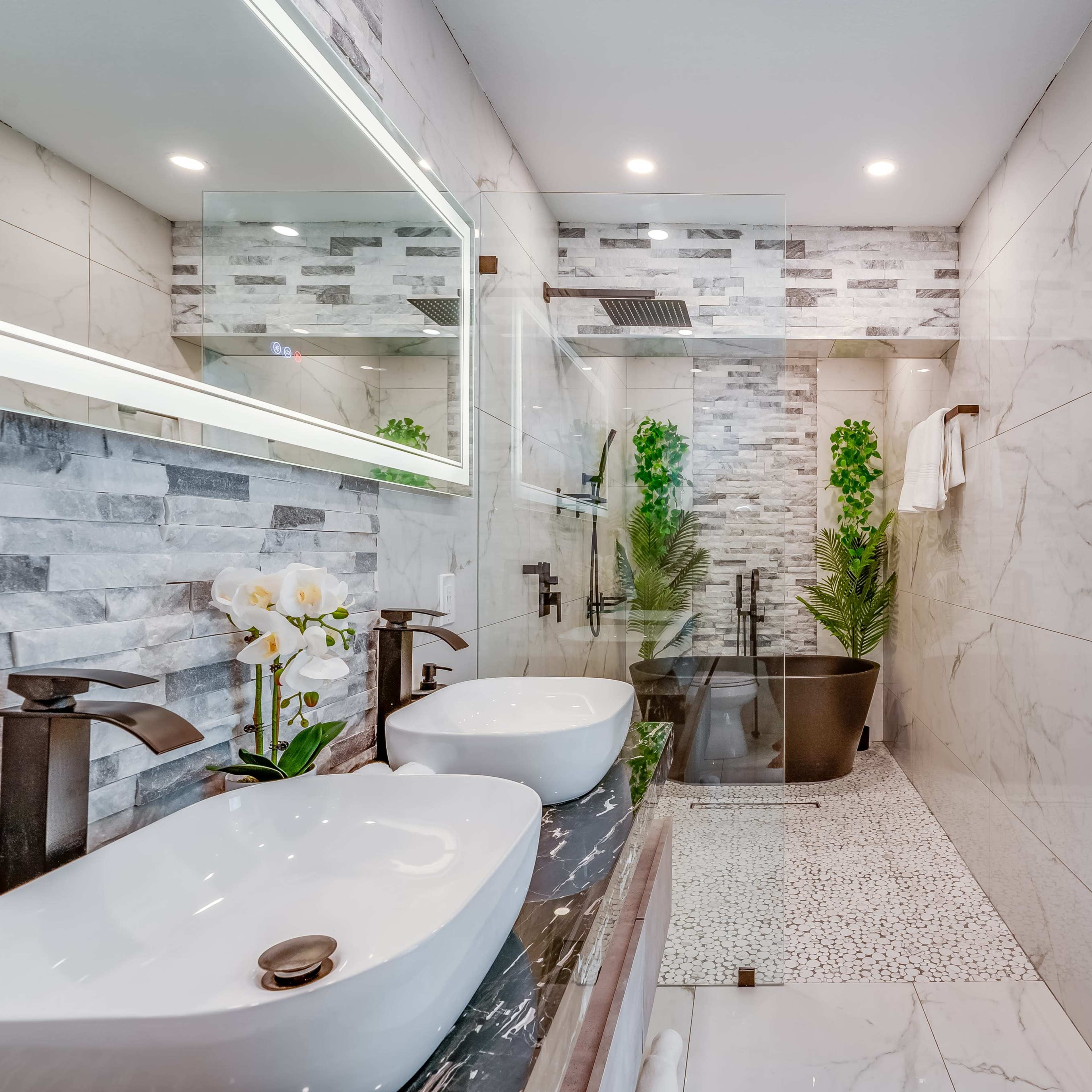 A modern bathroom featuring double sinks, a freestanding bathtub, and tile accents, complemented by greenery and natural light.