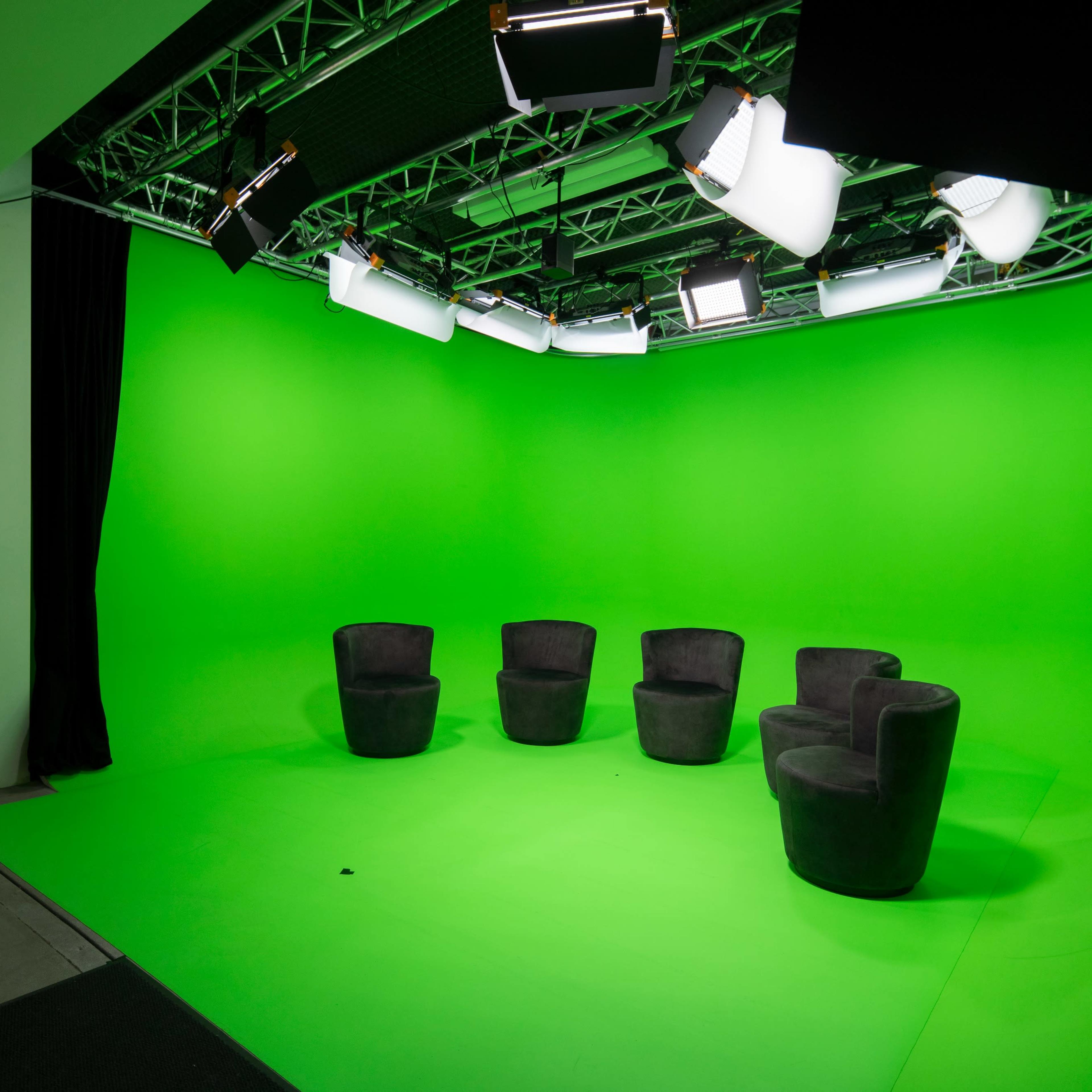 A studio setup with four black chairs arranged on a green screen backdrop and overhead lighting.