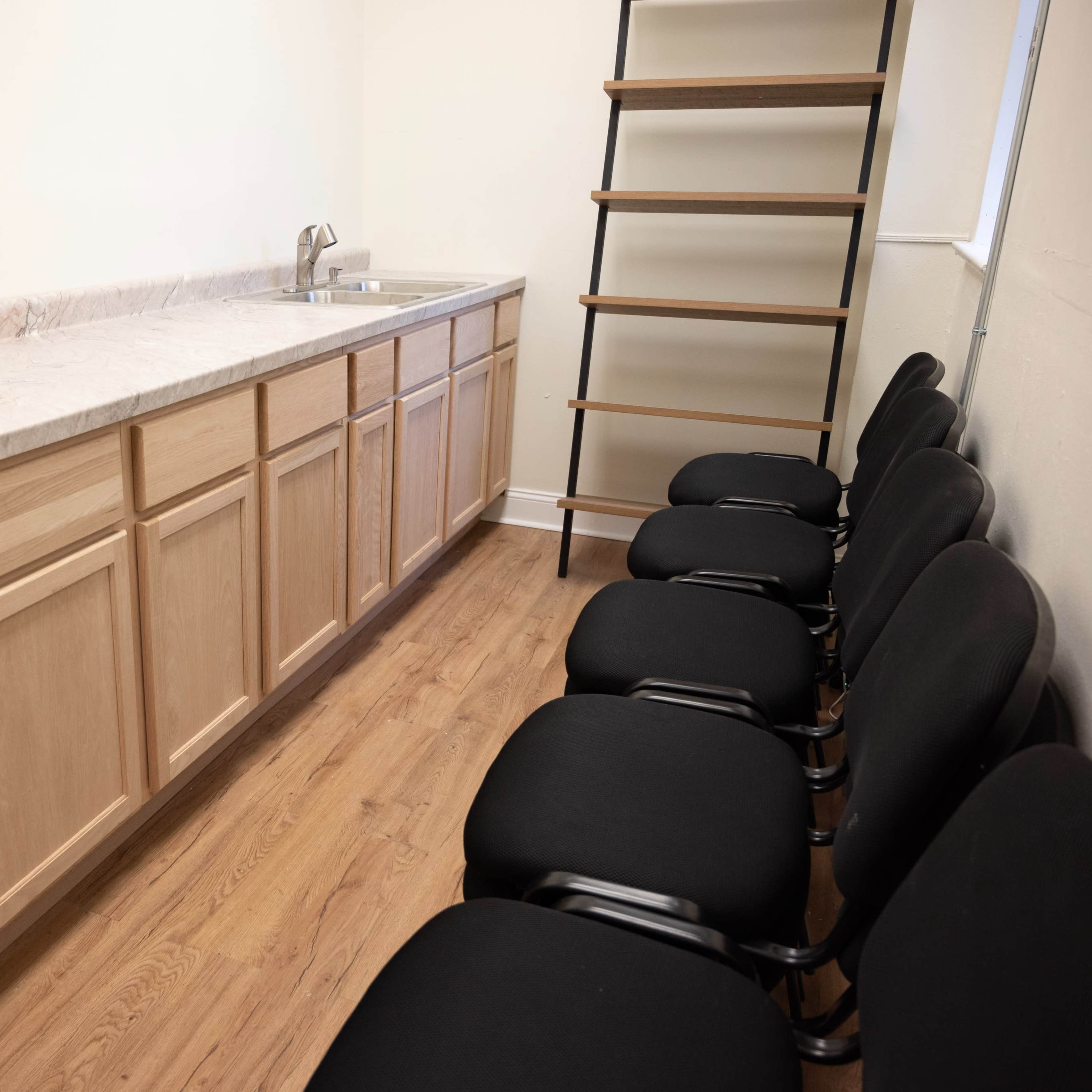 A kitchen area with a long countertop, a sink, and a row of black chairs along one side.