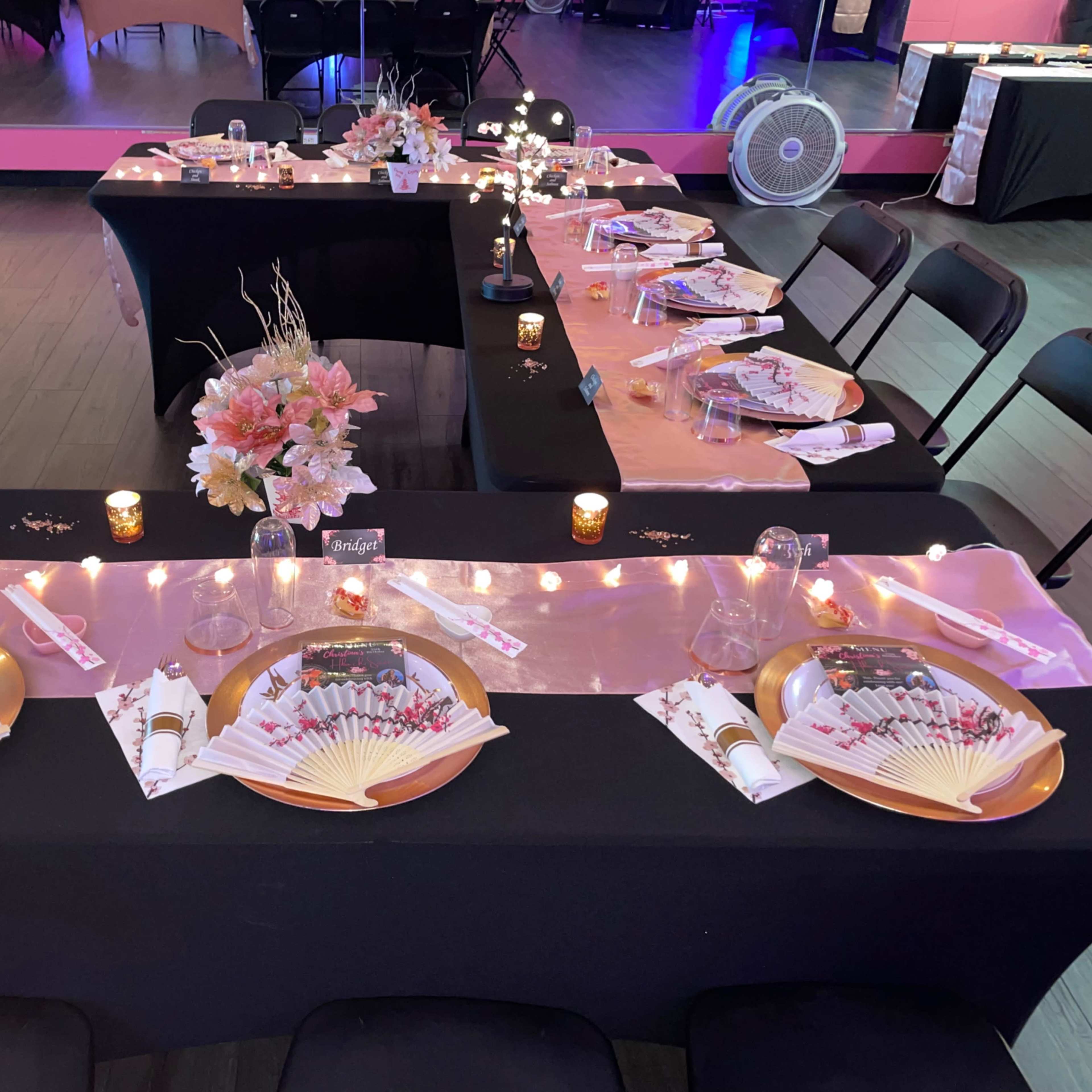 A banquet setup with black and pink tablecloths adorned with flower centerpieces, candles, and neatly arranged plates and utensils.