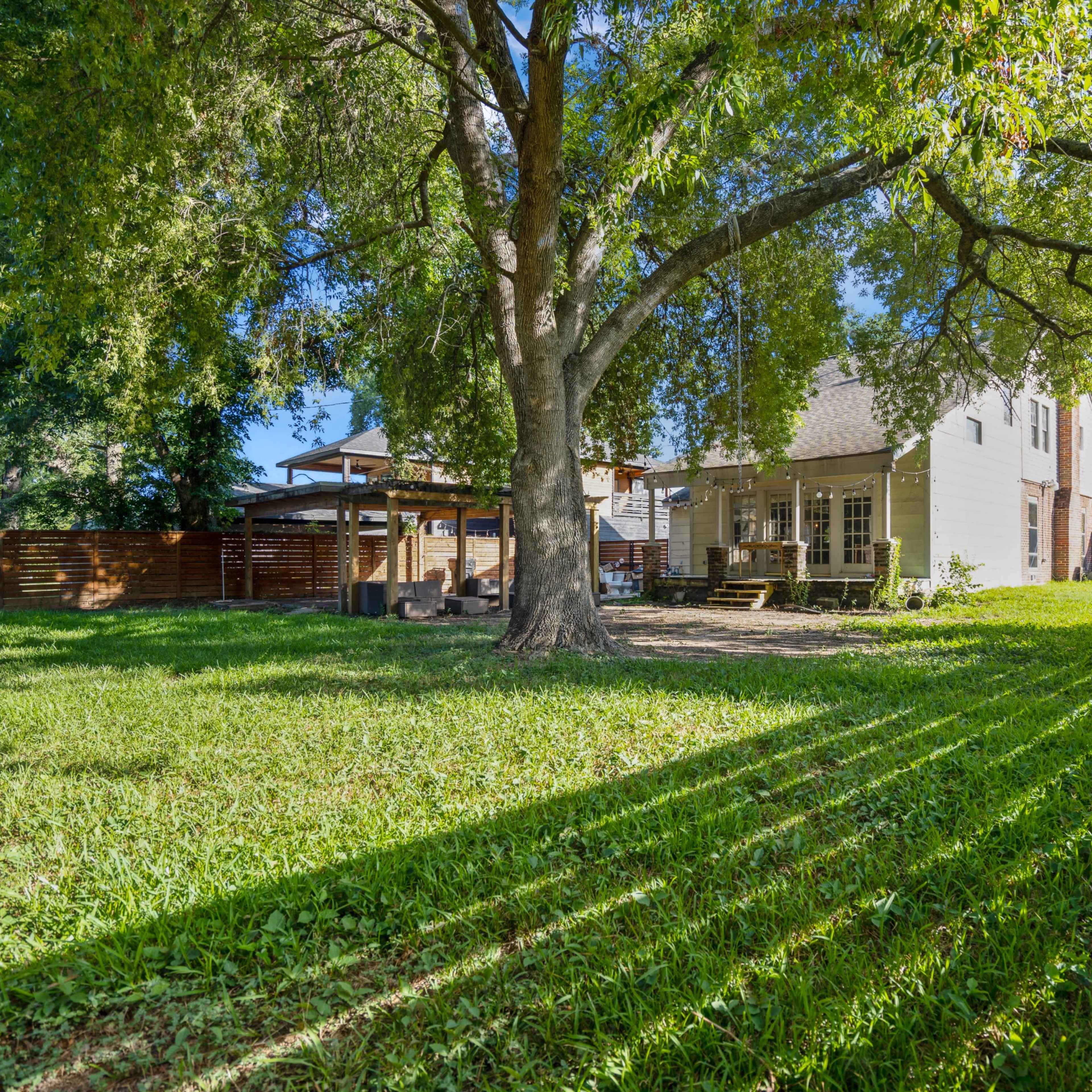 A spacious backyard features a large tree, well-maintained grass, and a house with a patio area visible in the background.