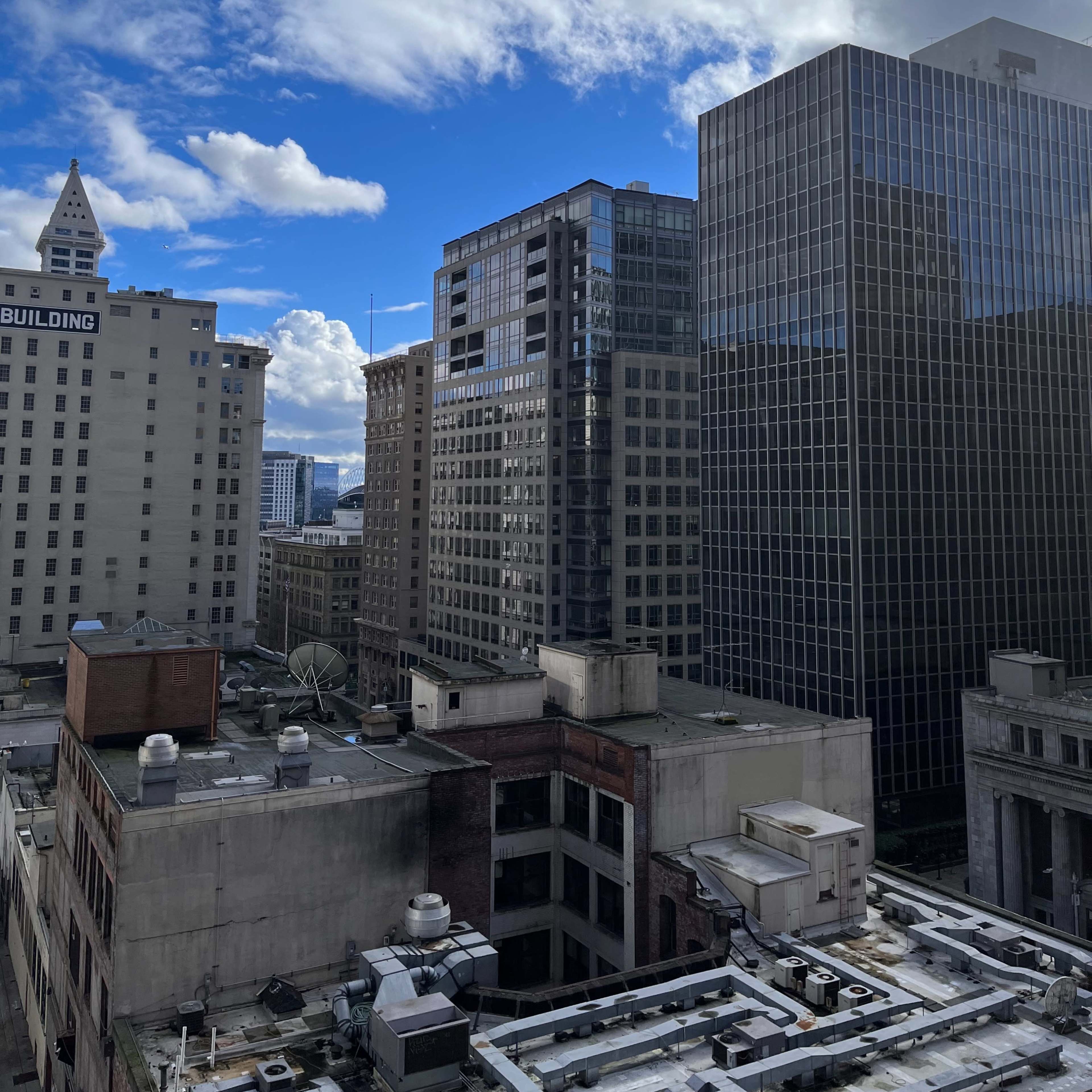 A cityscape with tall buildings, a clear blue sky, and scattered clouds.