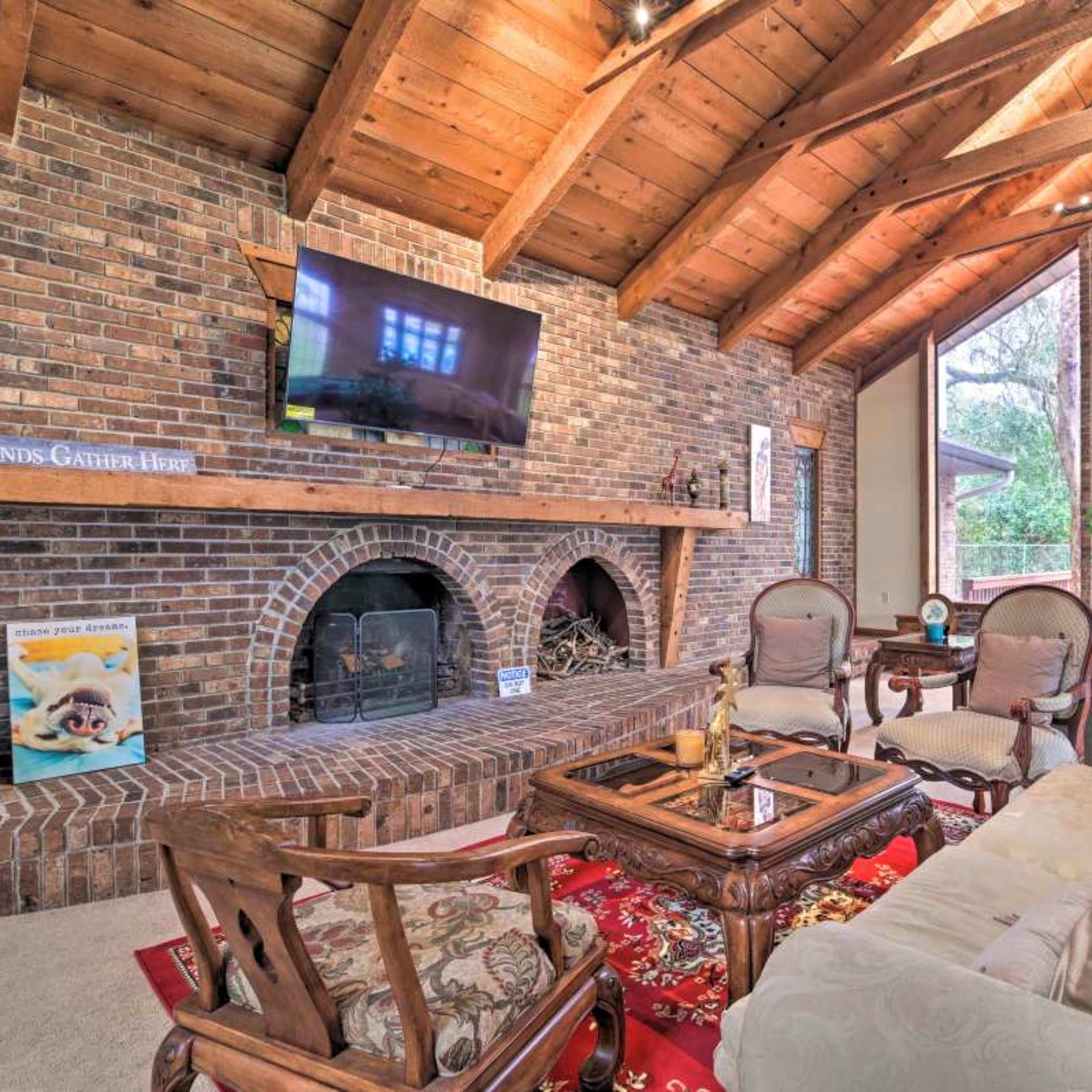 A living room with a brick wall, wooden ceiling beams, a fireplace, and comfortable seating arrangements.