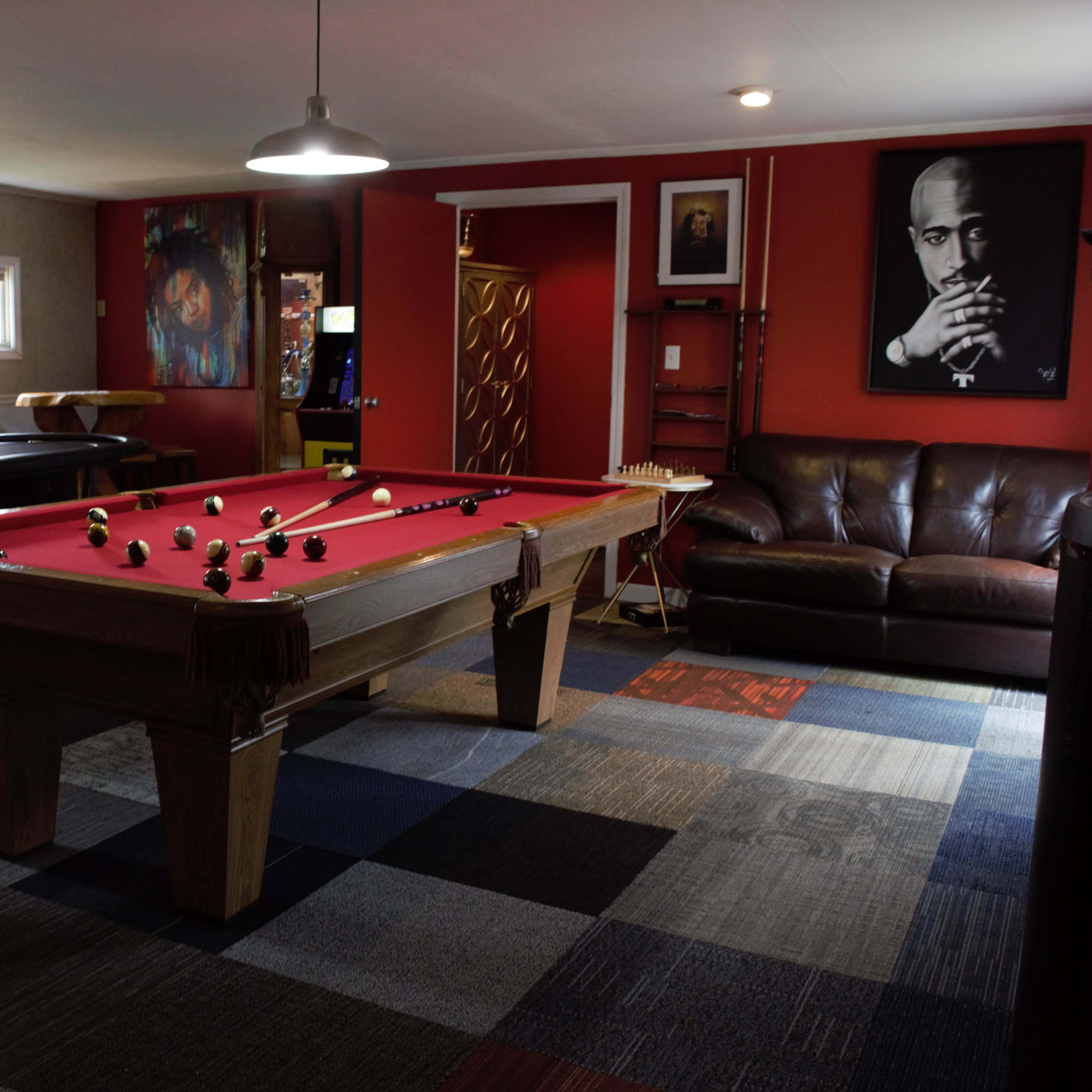 A game room featuring a red pool table, a leather couch, and several pieces of wall art, including portraits.