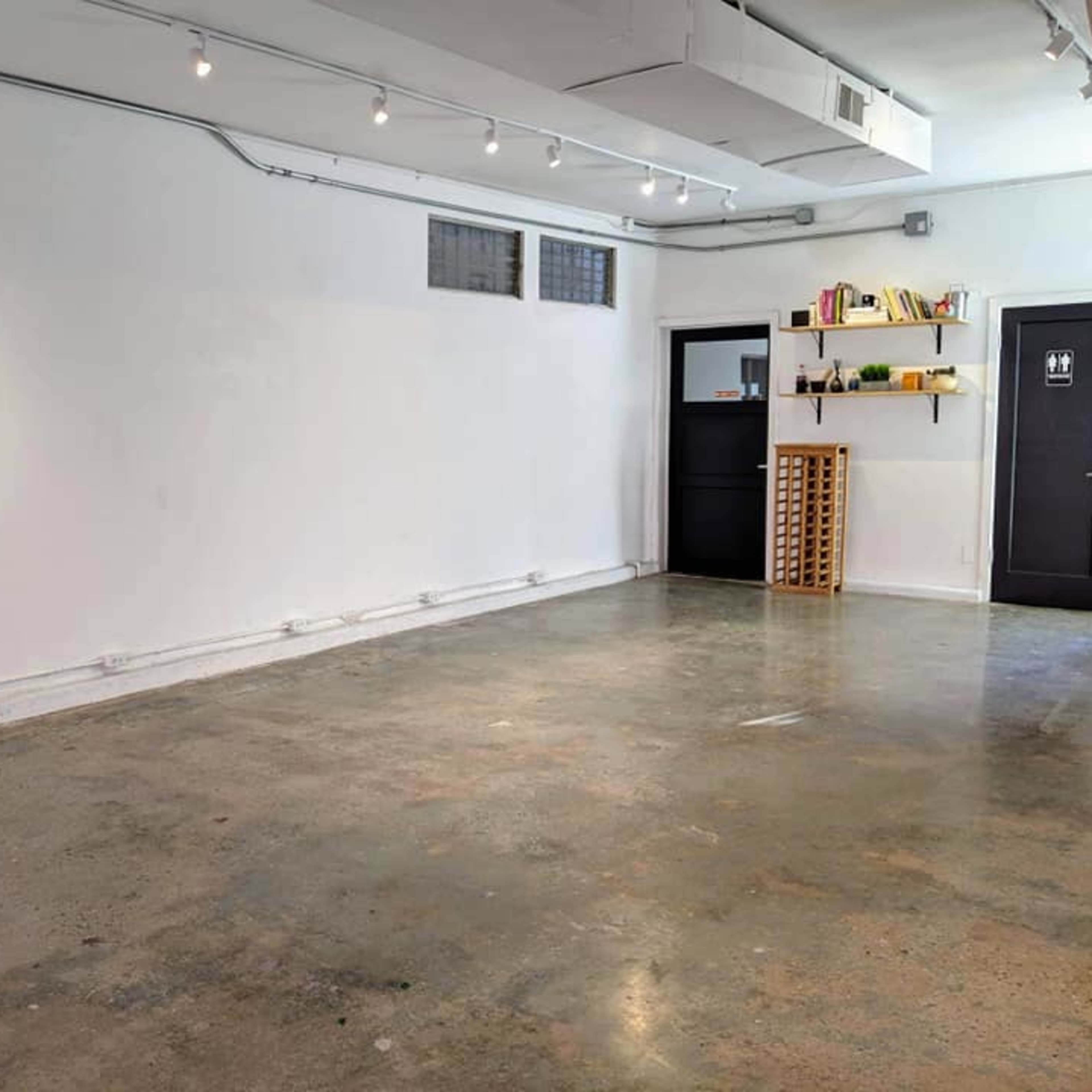 A spacious, empty room with polished concrete flooring, white walls, and a shelf containing books and decor on one side.