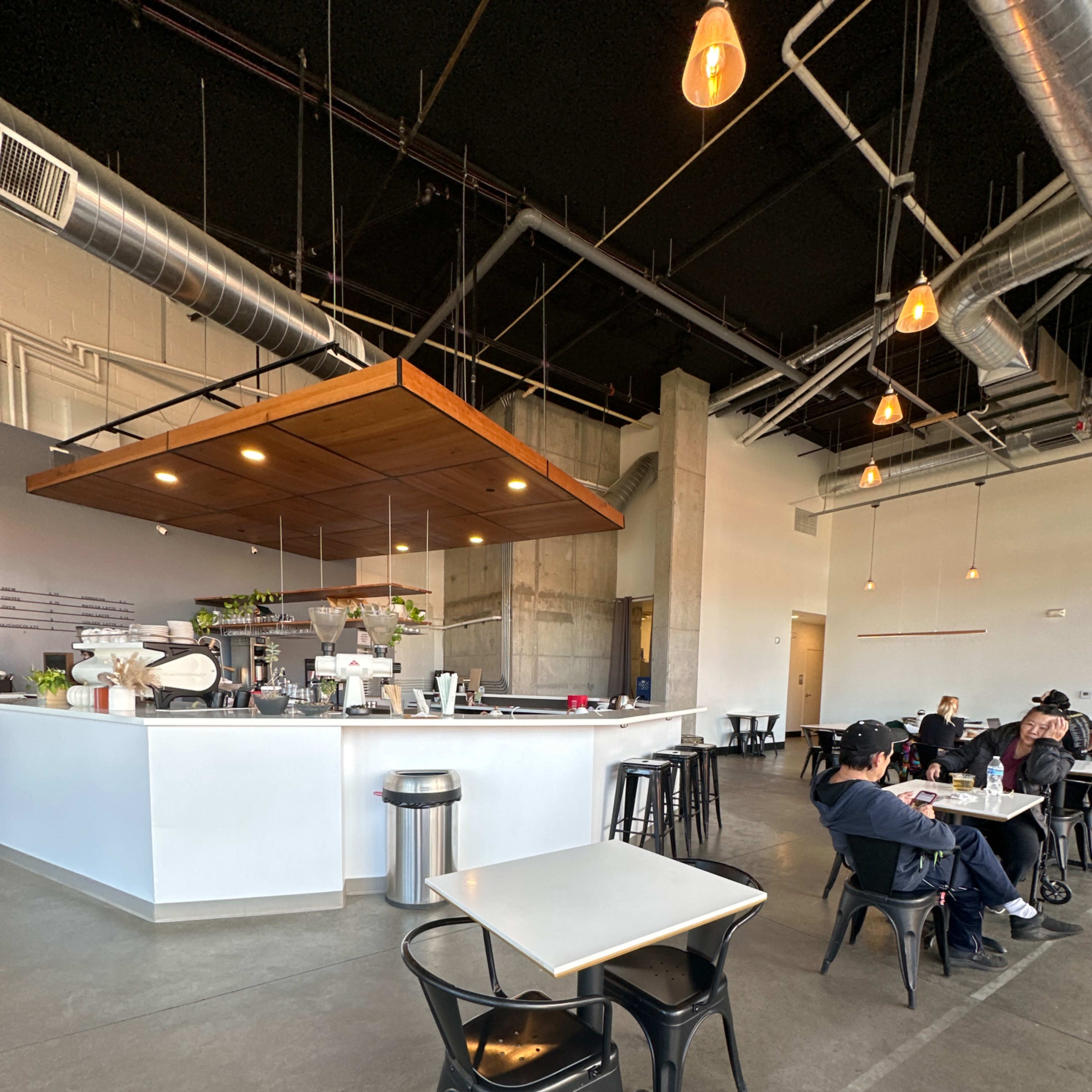 A modern café interior with a central service counter, minimalist furniture, and patrons seated at tables.