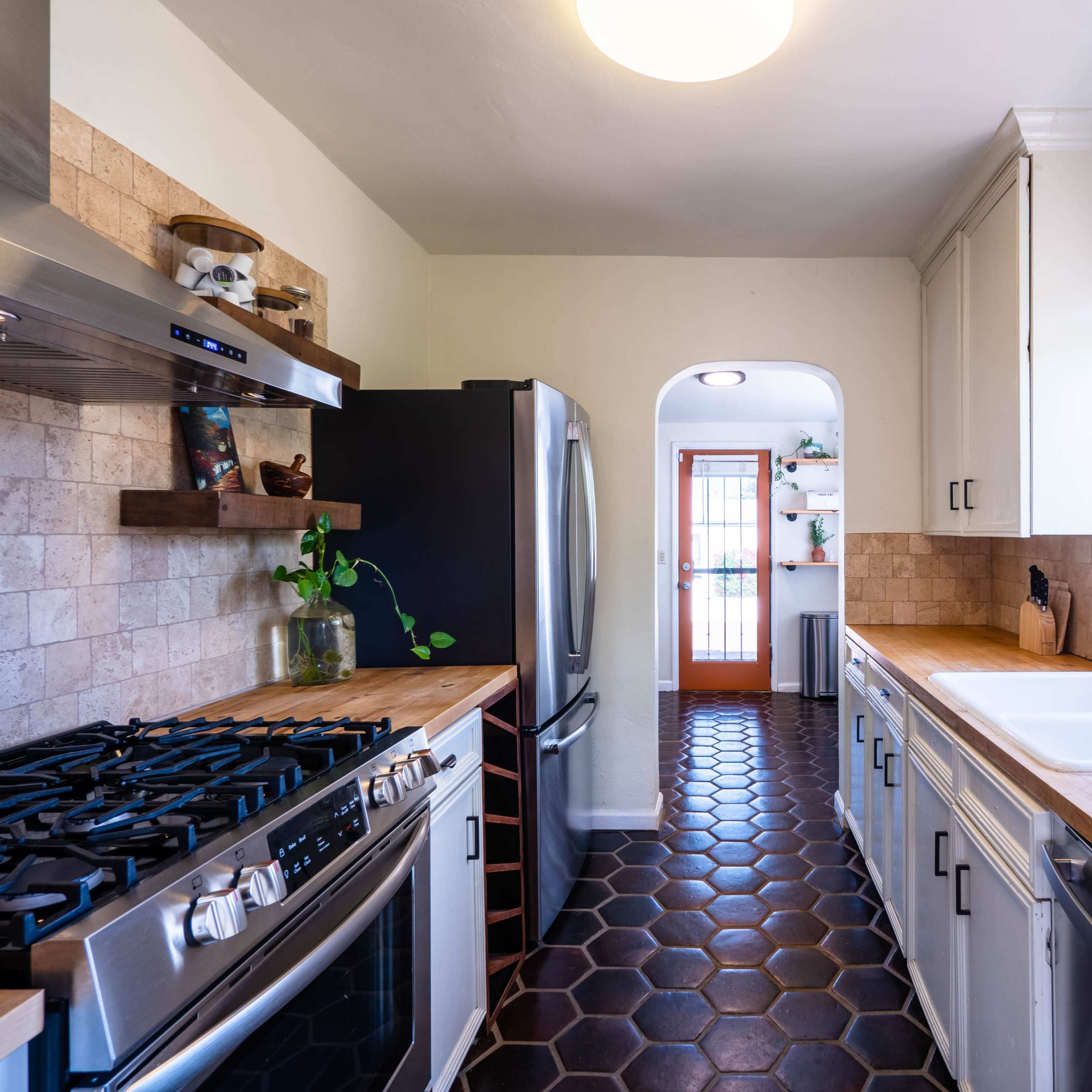 The kitchen features a gas stove, a stainless steel refrigerator, and a sink with wooden countertops, all arranged along tiled flooring.