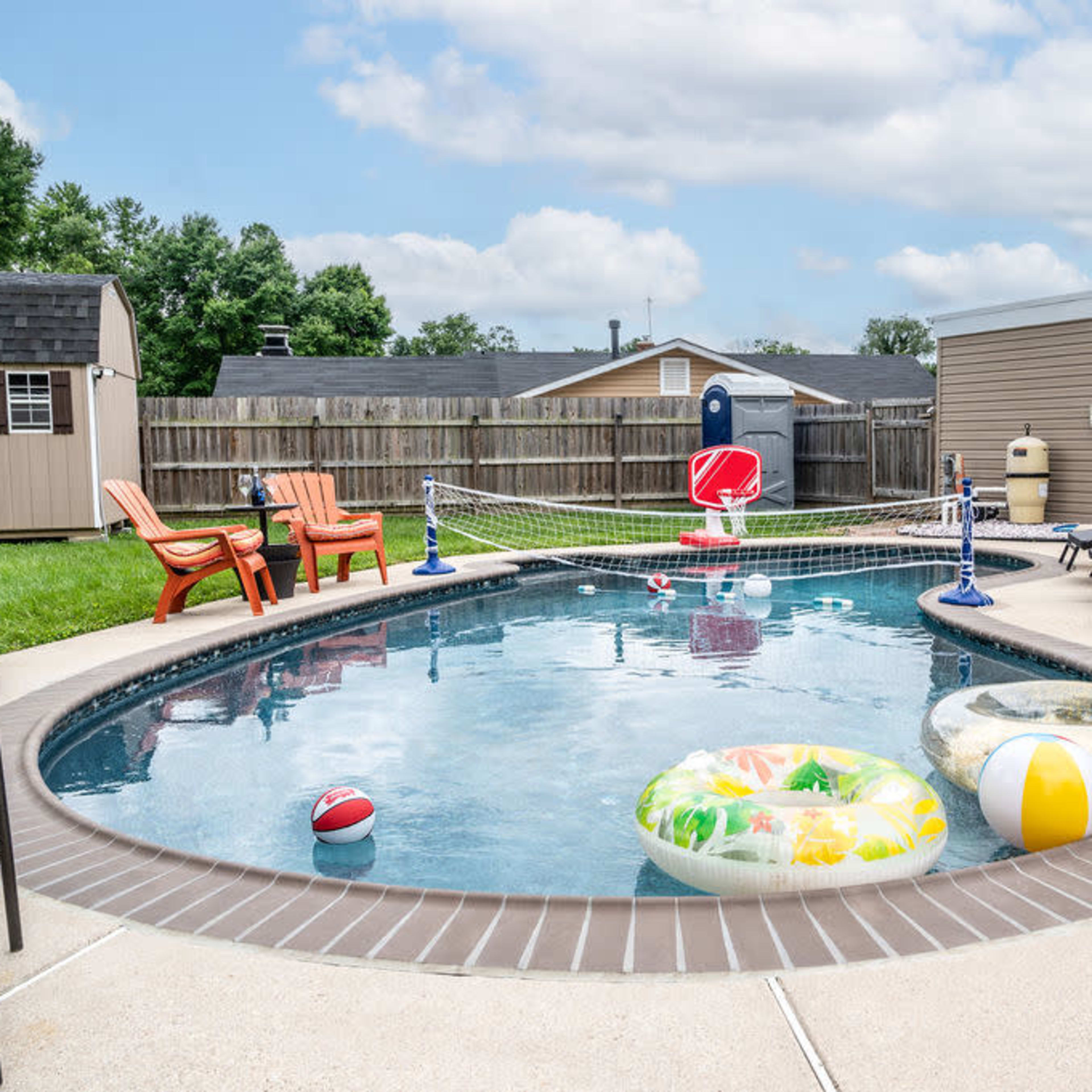 A backyard swimming pool surrounded by lounge chairs and colorful pool floats on a sunny day.