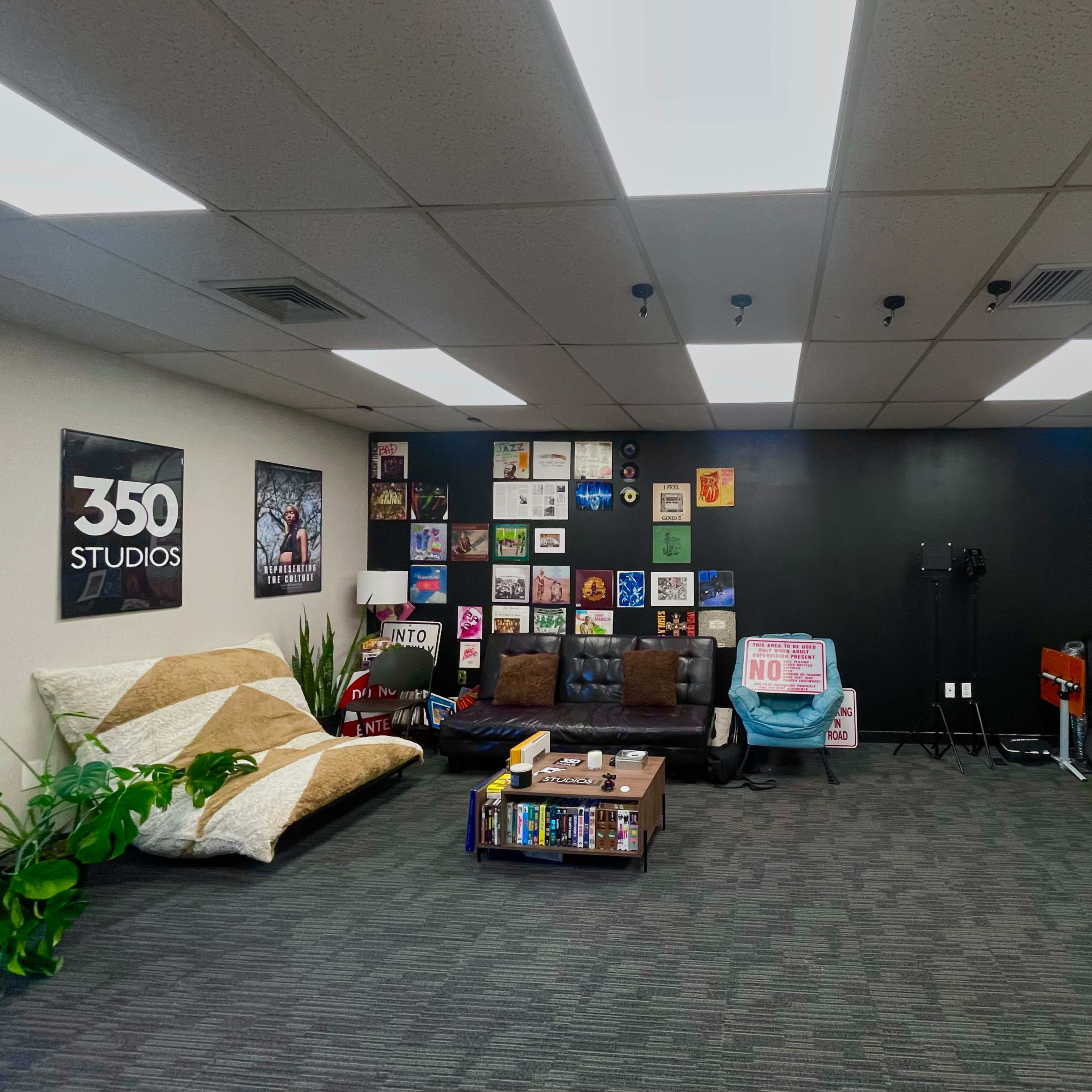 A studio space with a dark accent wall adorned with various framed art pieces, a brown couch, a patterned rug, and several studio equipment items arranged along the sides.