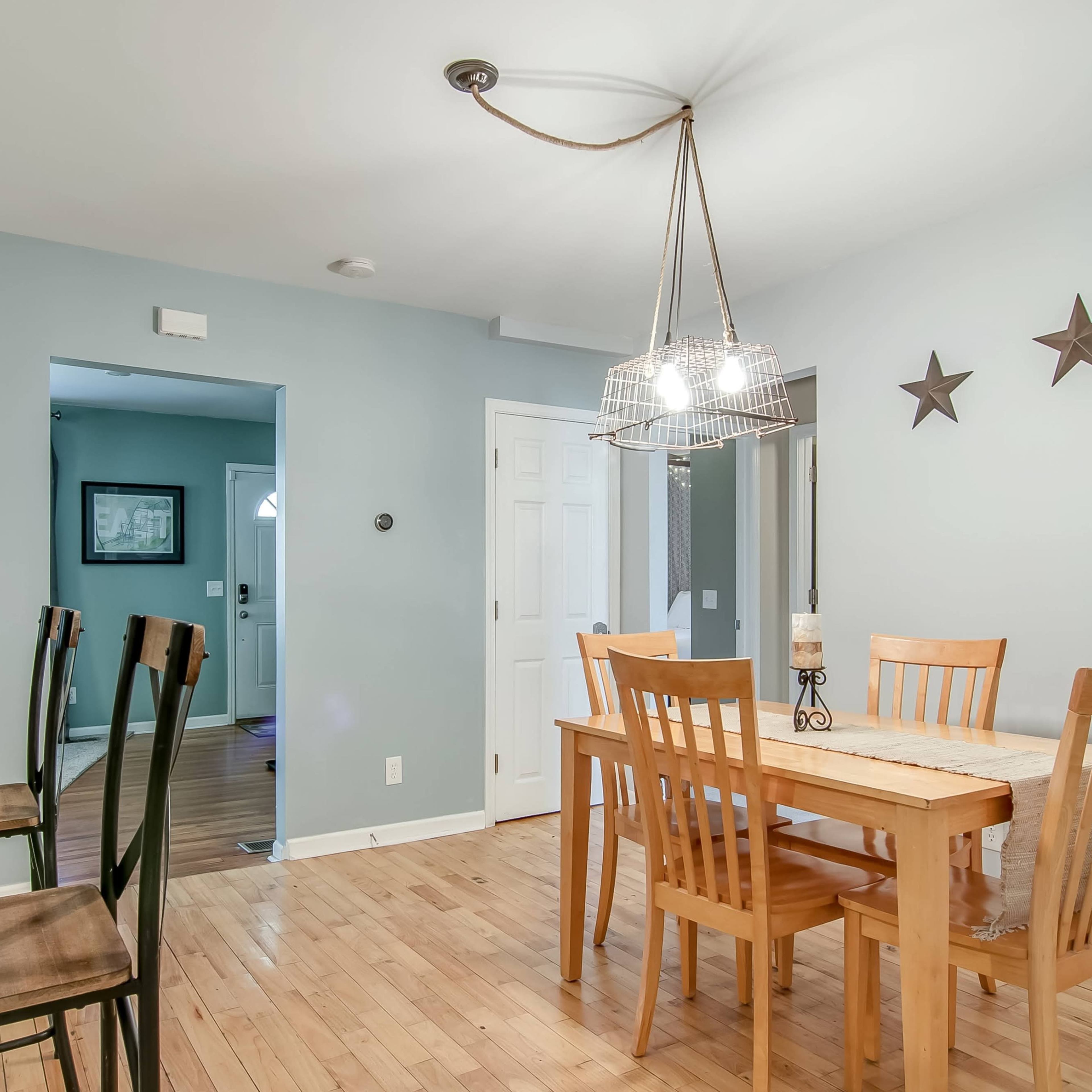 A dining area features a wooden table surrounded by six chairs, with a light fixture overhead and three decorative stars on the wall.