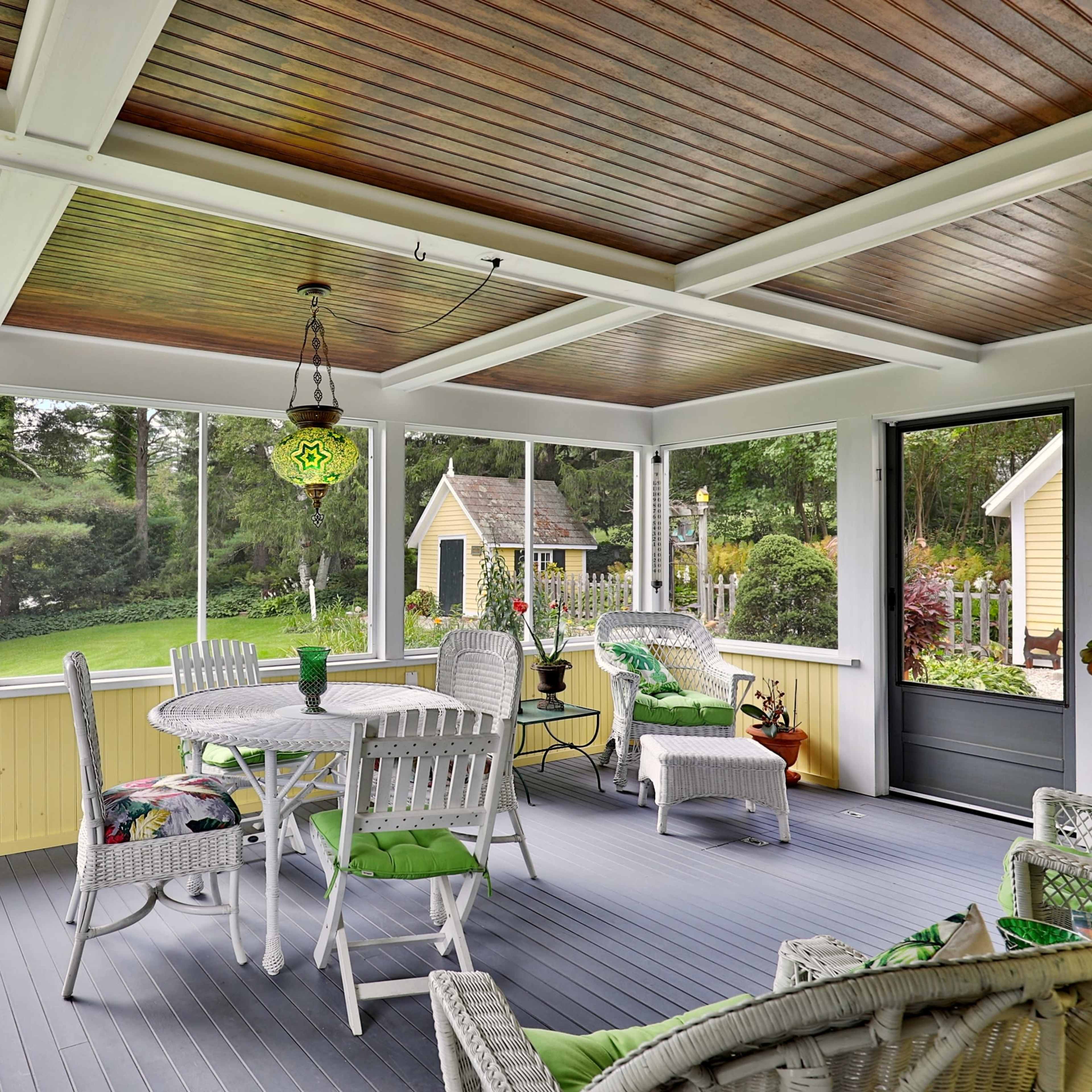 A screened-in porch with wicker furniture, a round table, and a green lawn visible through the open screens.