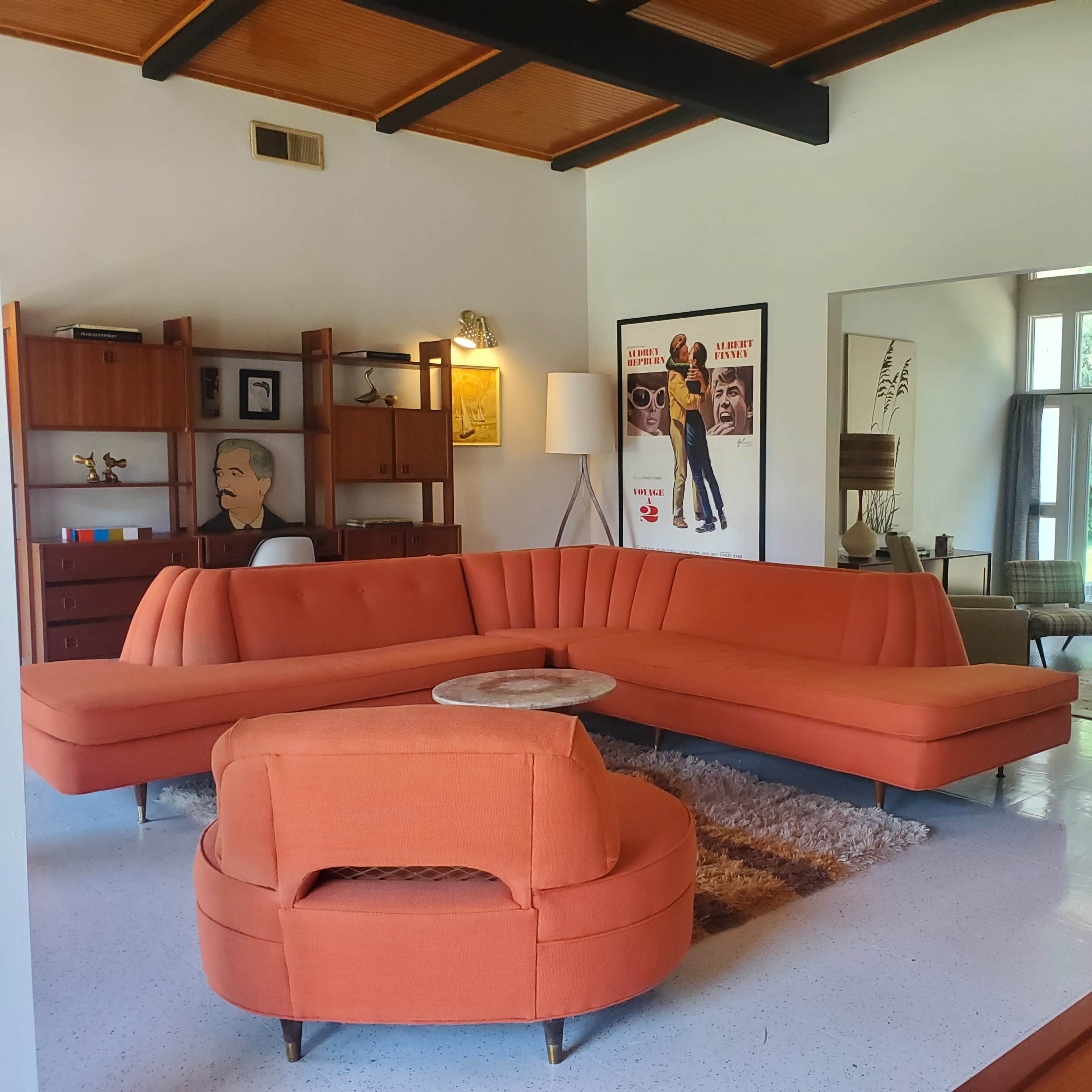A modern living room with an orange sectional sofa, a round coffee table, artwork on the walls, and large windows providing natural light.