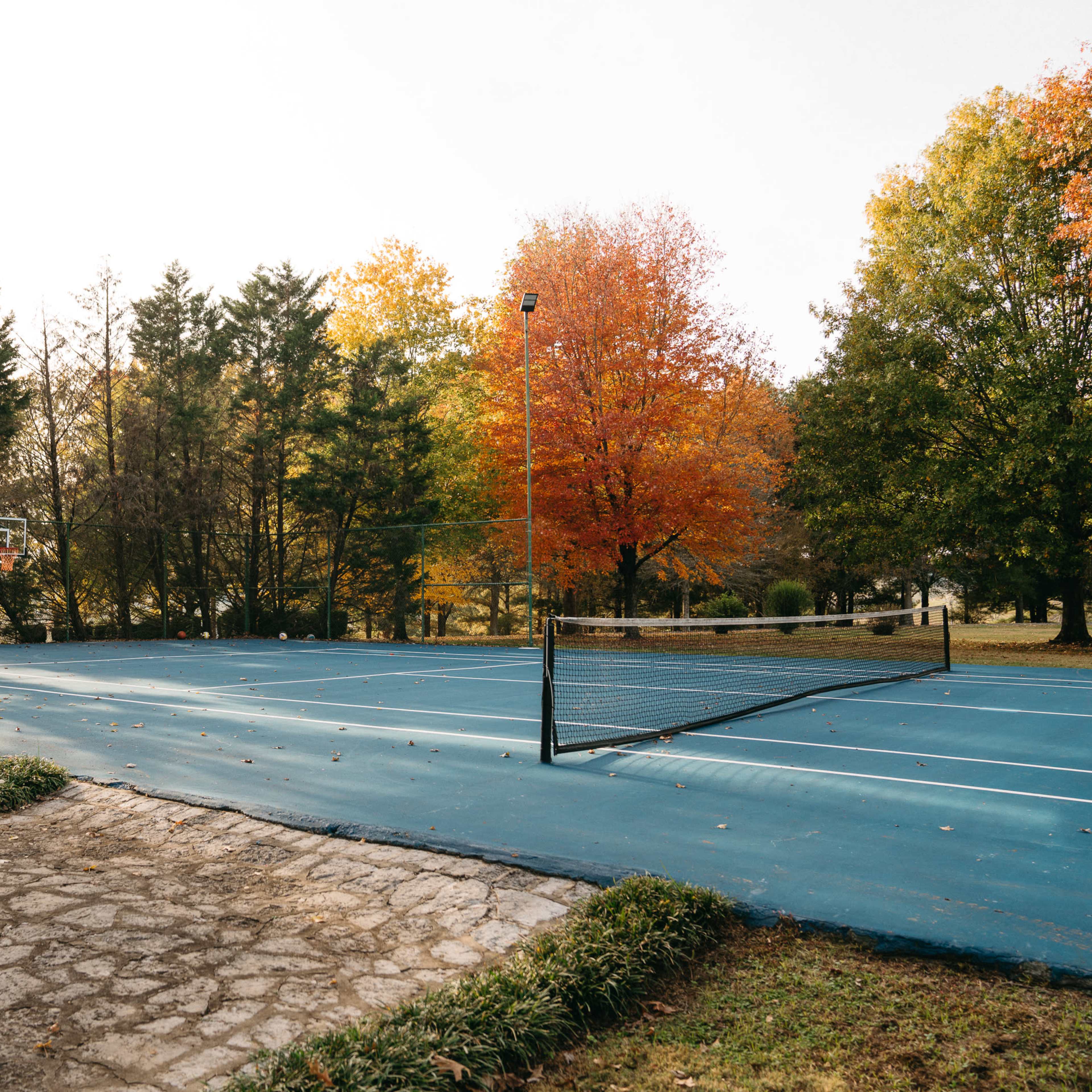 An empty outdoor basketball court is surrounded by trees with autumn foliage.
