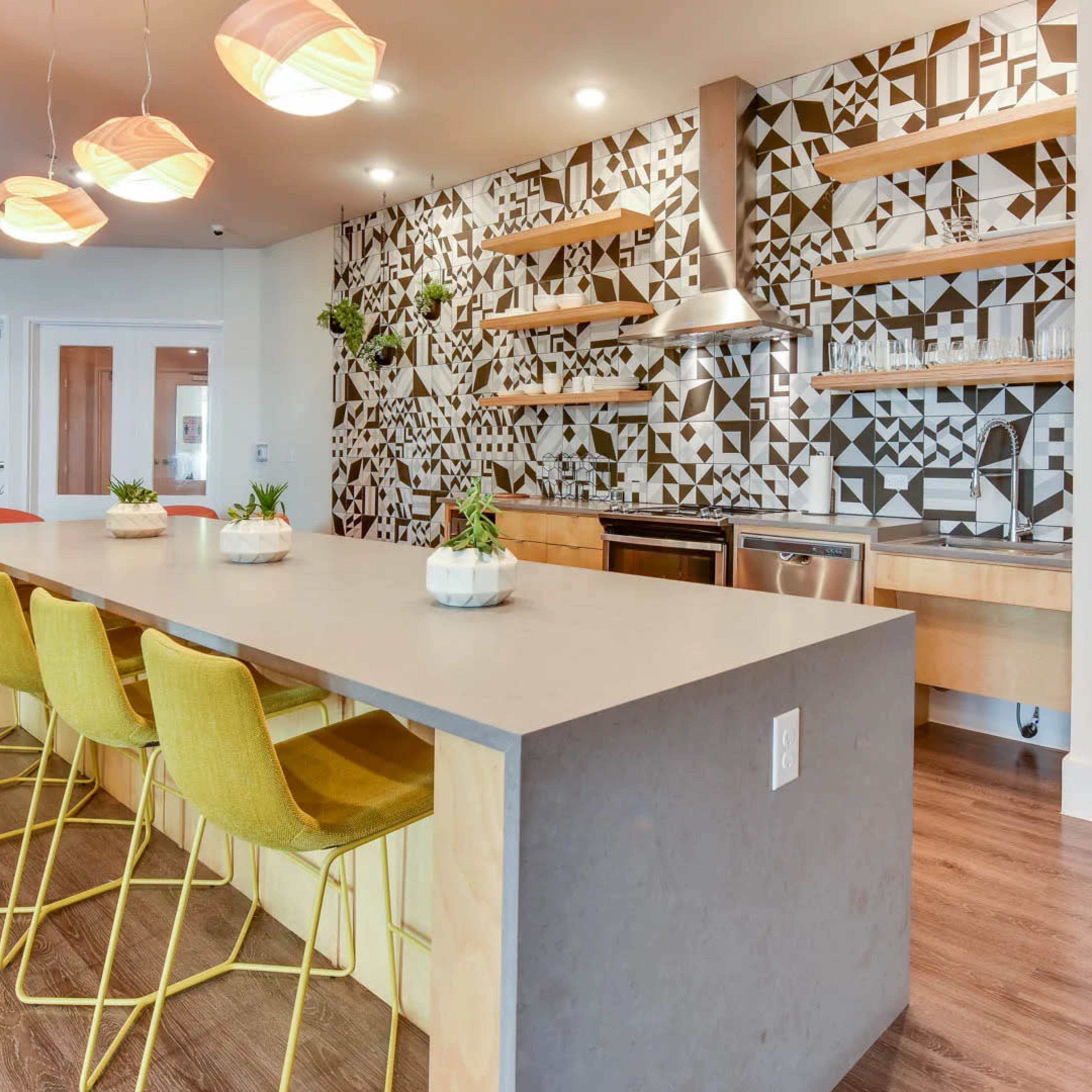 A modern kitchen with a geometric-patterned backsplash, a central island with yellow bar stools, and stainless steel appliances.