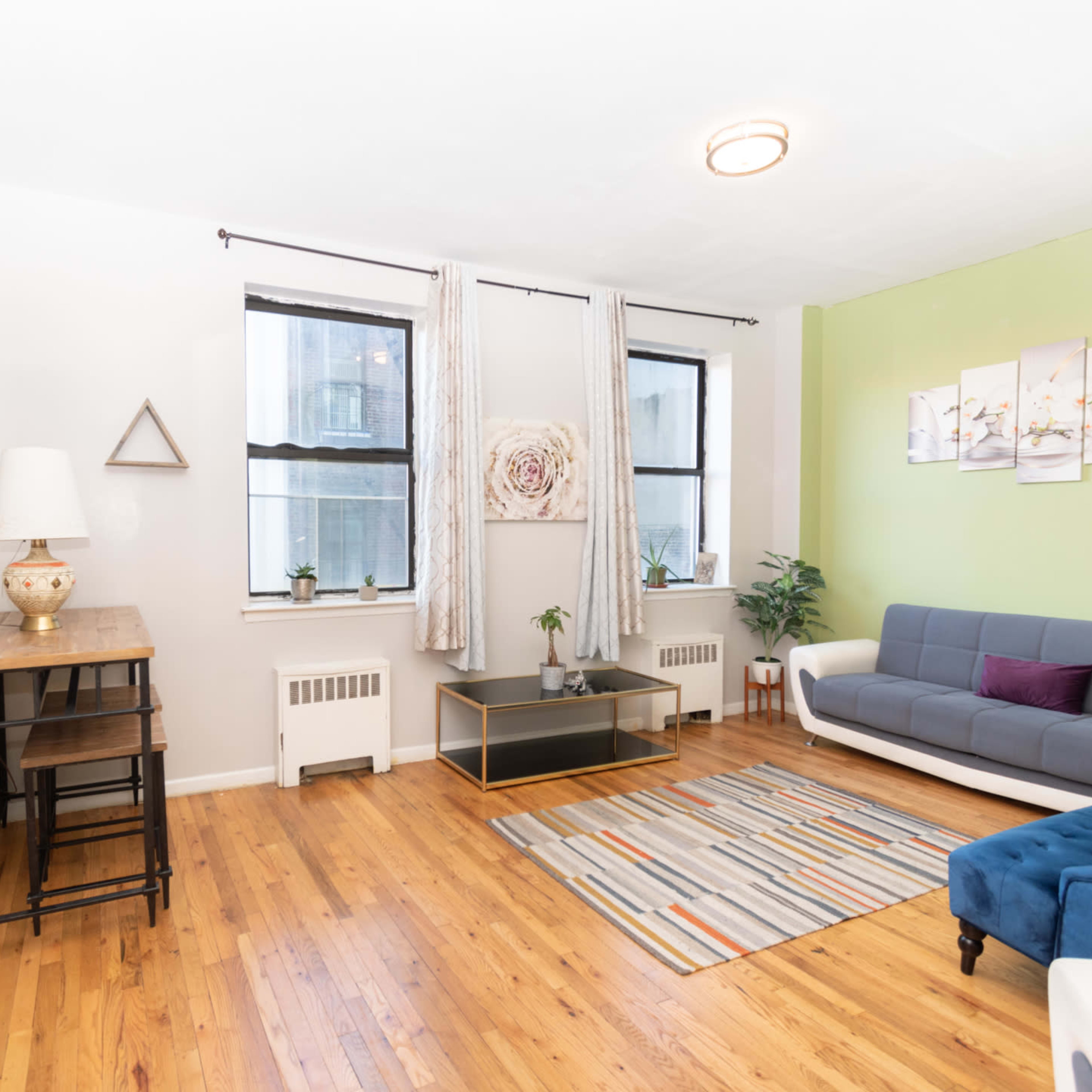 A living room featuring a blue sofa, a wooden table, large windows, and hardwood flooring.