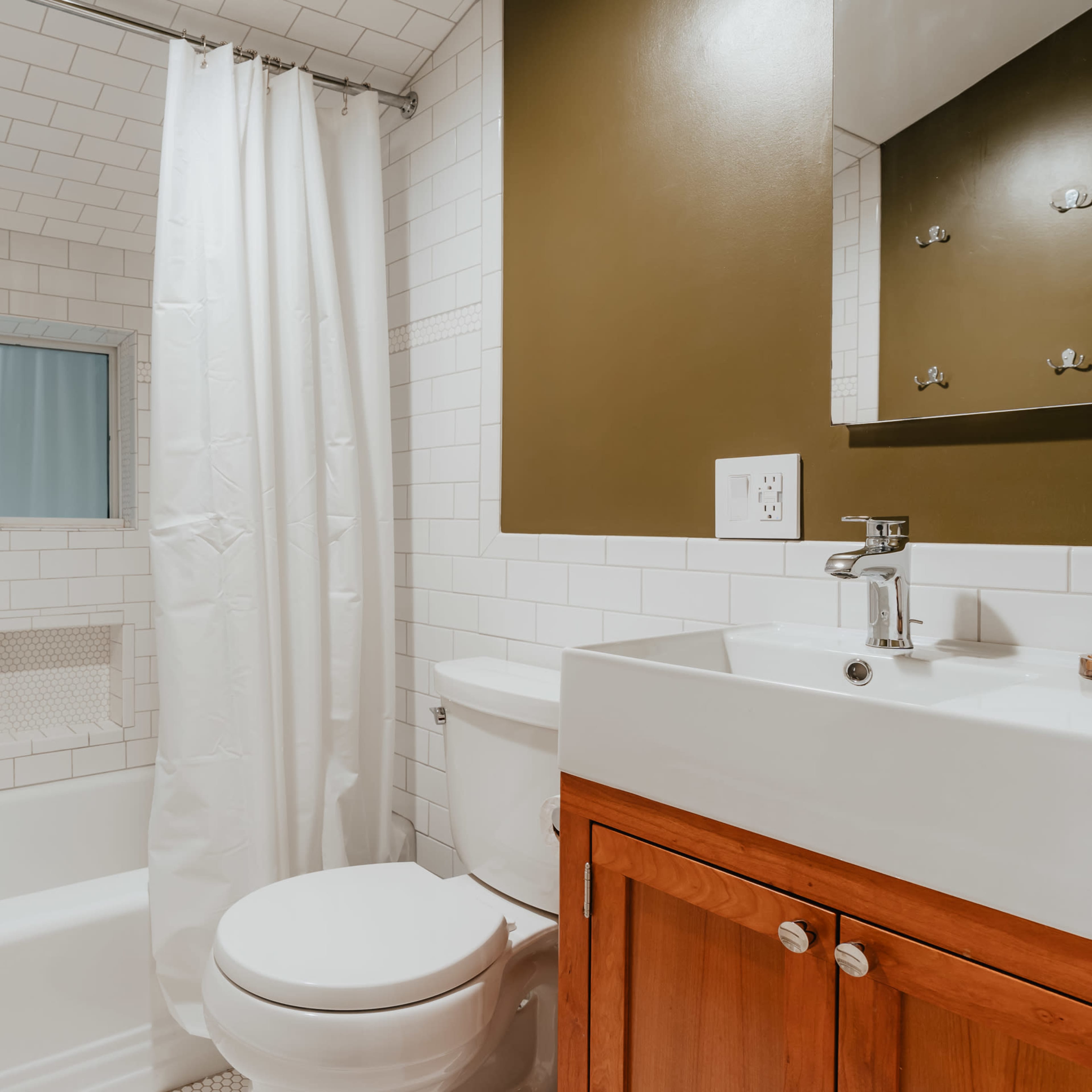 A modern bathroom featuring a bathtub with a shower curtain, a wall-mounted mirror, and a wooden vanity with a sink.
