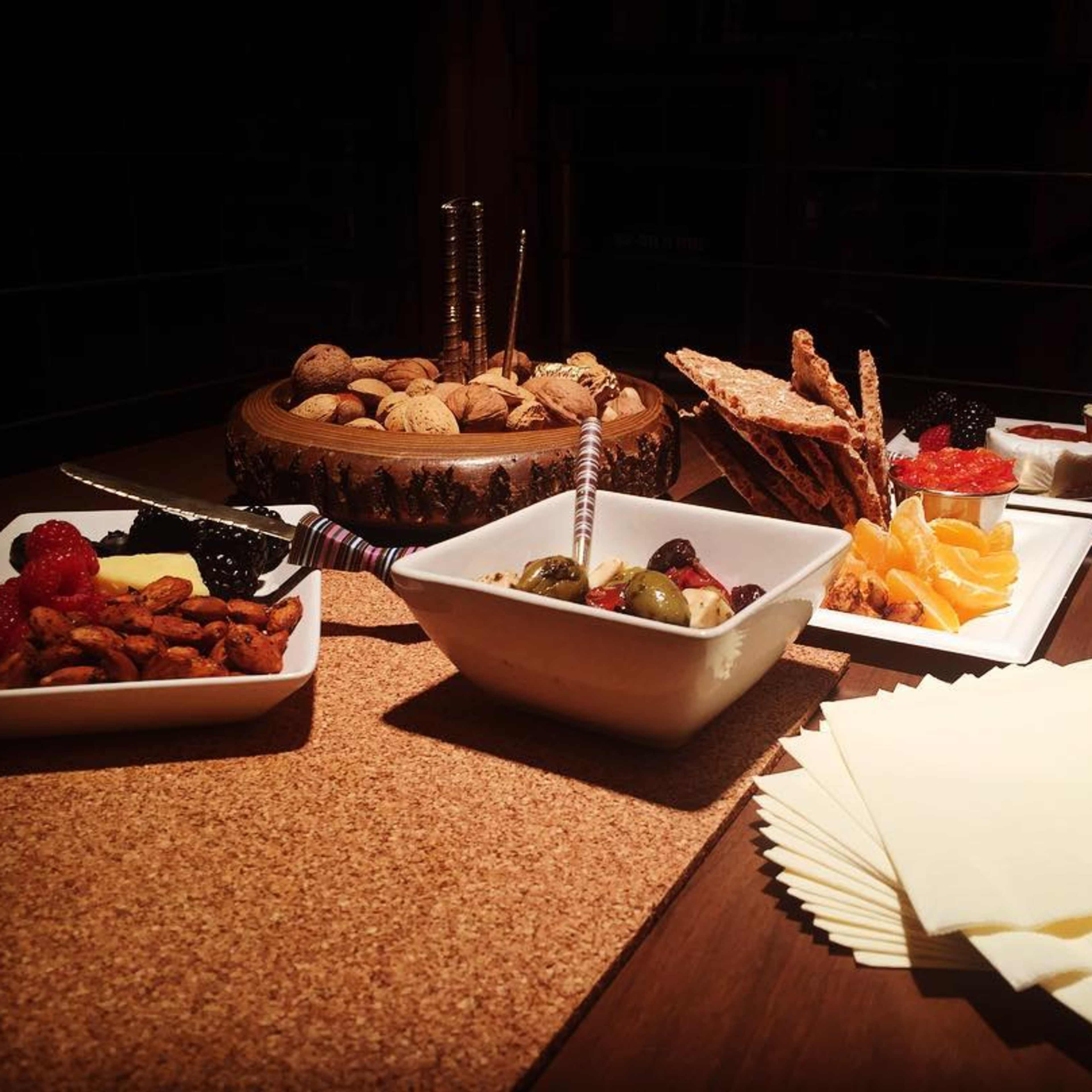 A variety of snacks arranged on a wooden table, including nuts, olives, fruits, and crackers, accompanied by paper napkins.