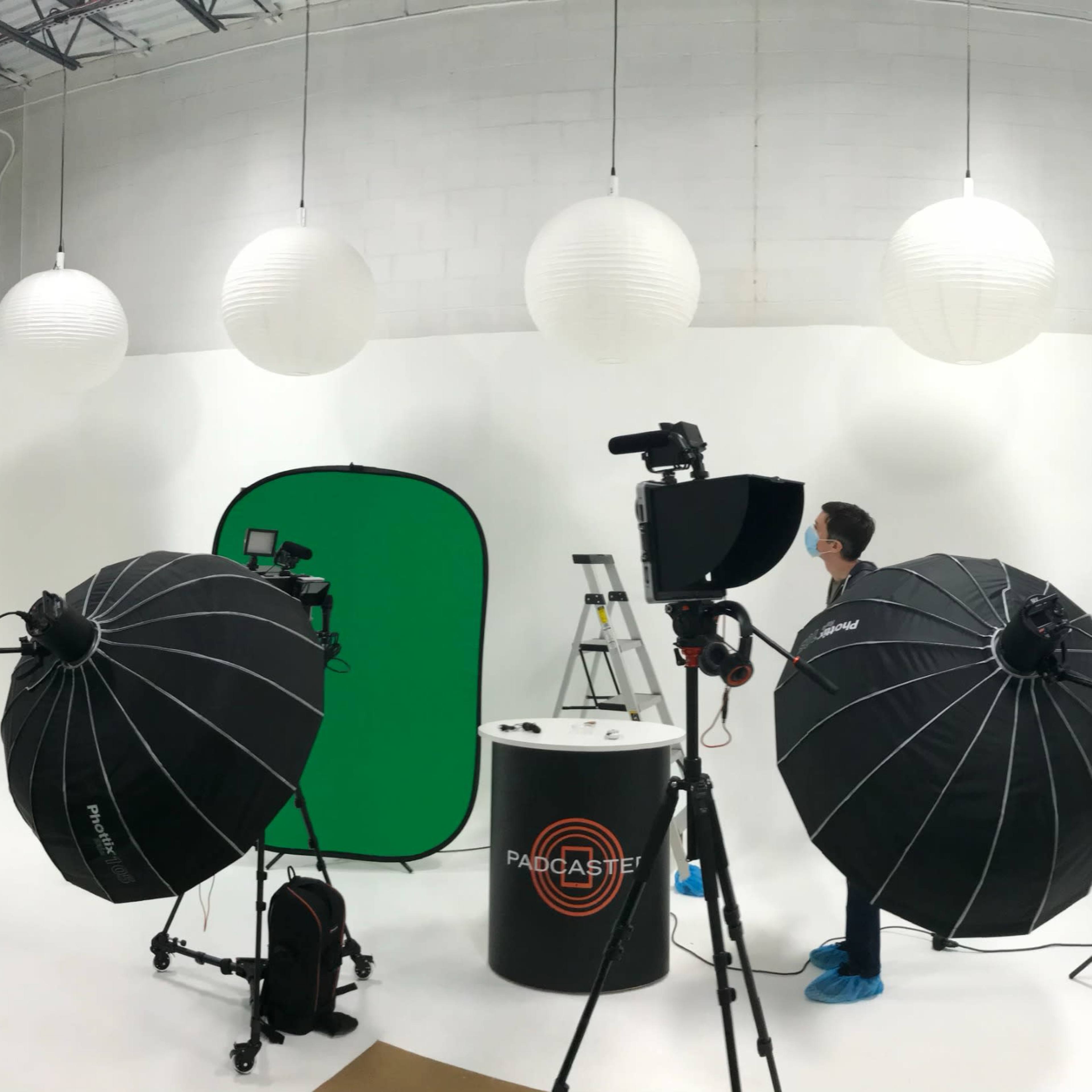 A photography studio features a green screen setup, softbox lighting, and paper lanterns hanging from the ceiling.