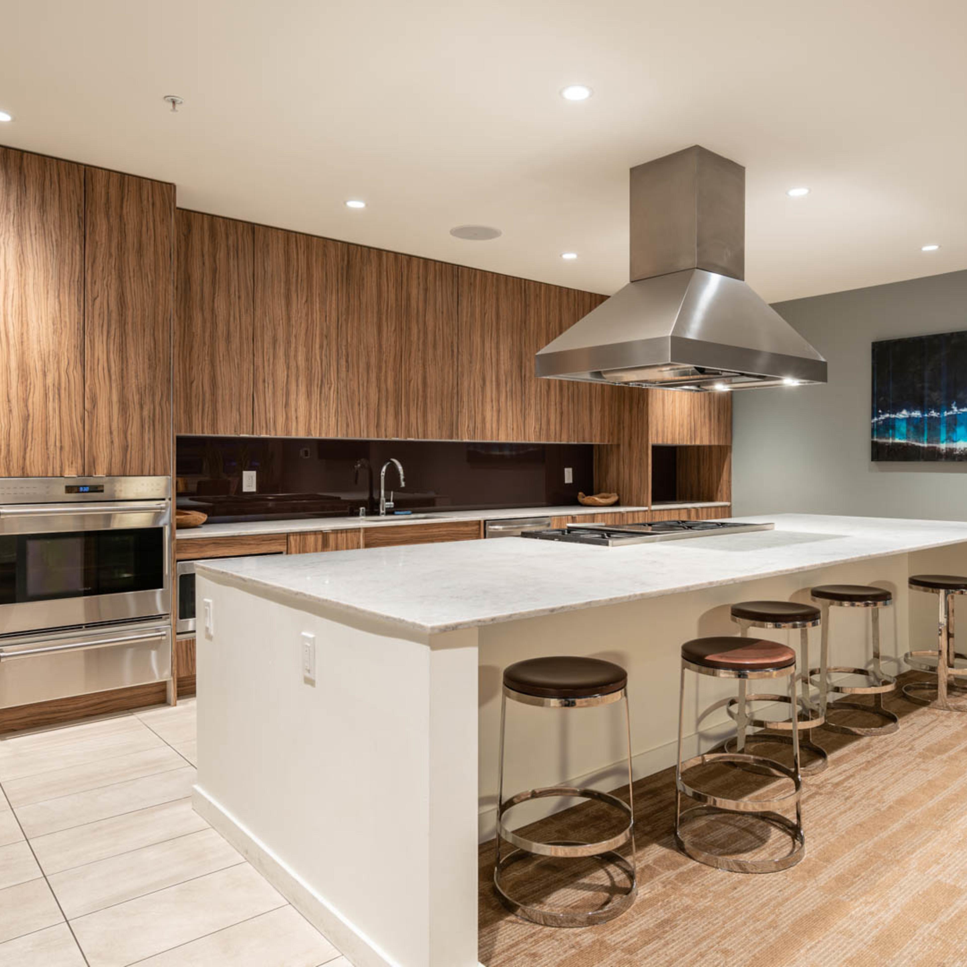 A modern kitchen featuring a large island with bar stools, stainless steel appliances, and wooden cabinetry.
