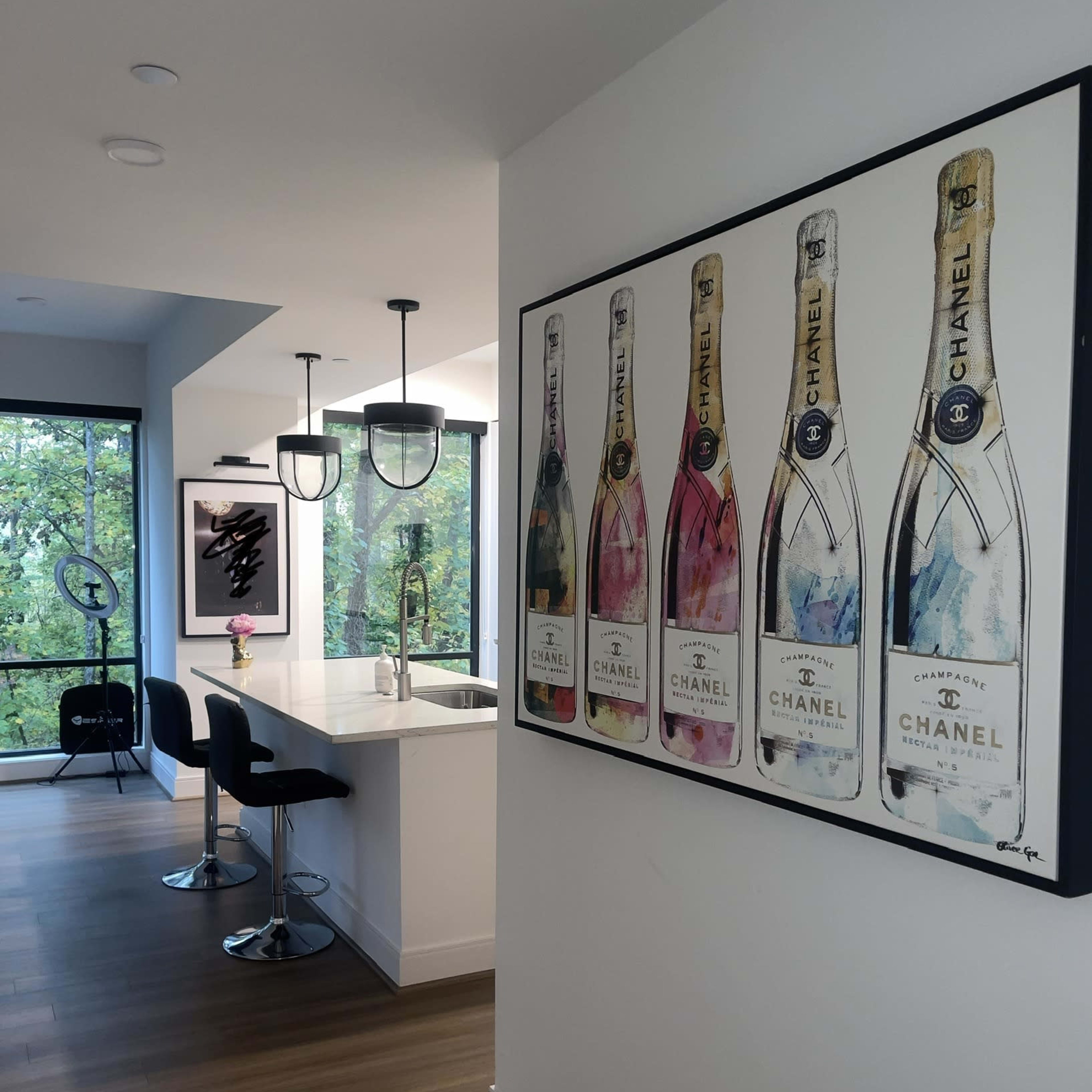 A modern kitchen with a bar area featuring black stools and a large framed artwork of champagne bottles on the wall.