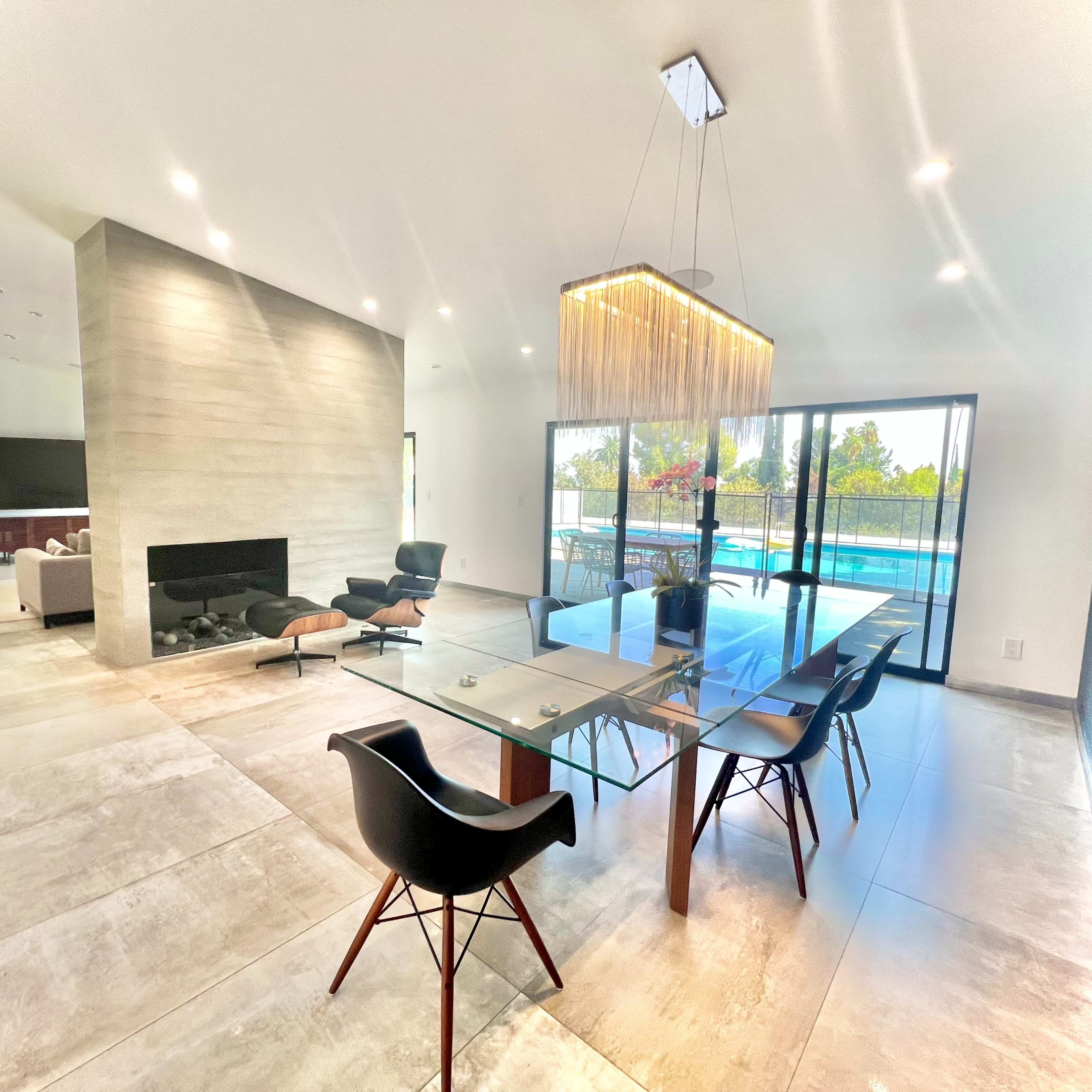 A modern dining area featuring a glass table with black chairs, a stone wall, and a large window overlooking a pool.