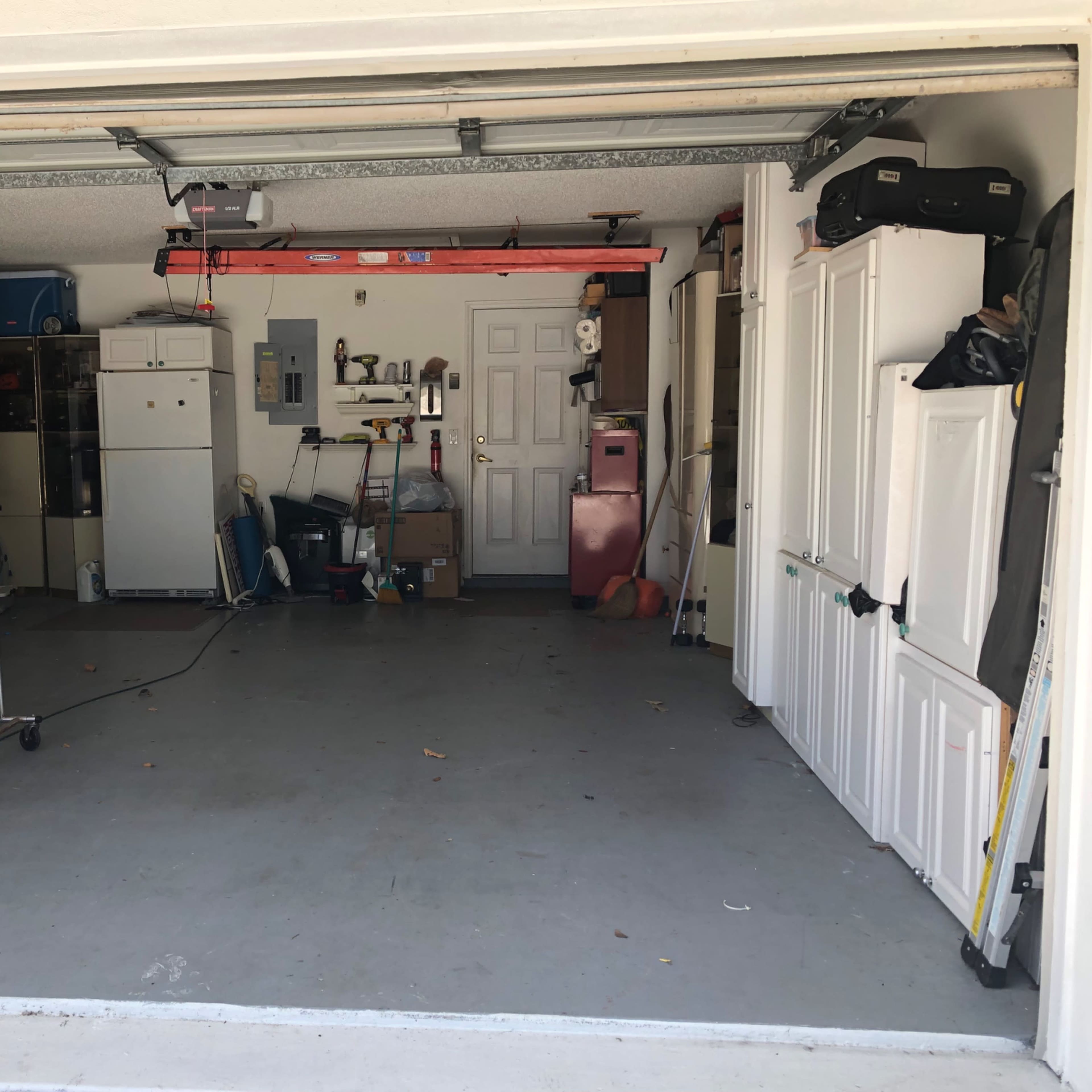 A spacious garage with various storage items, including a refrigerator, shelves, and hanging clothes racks along one side.