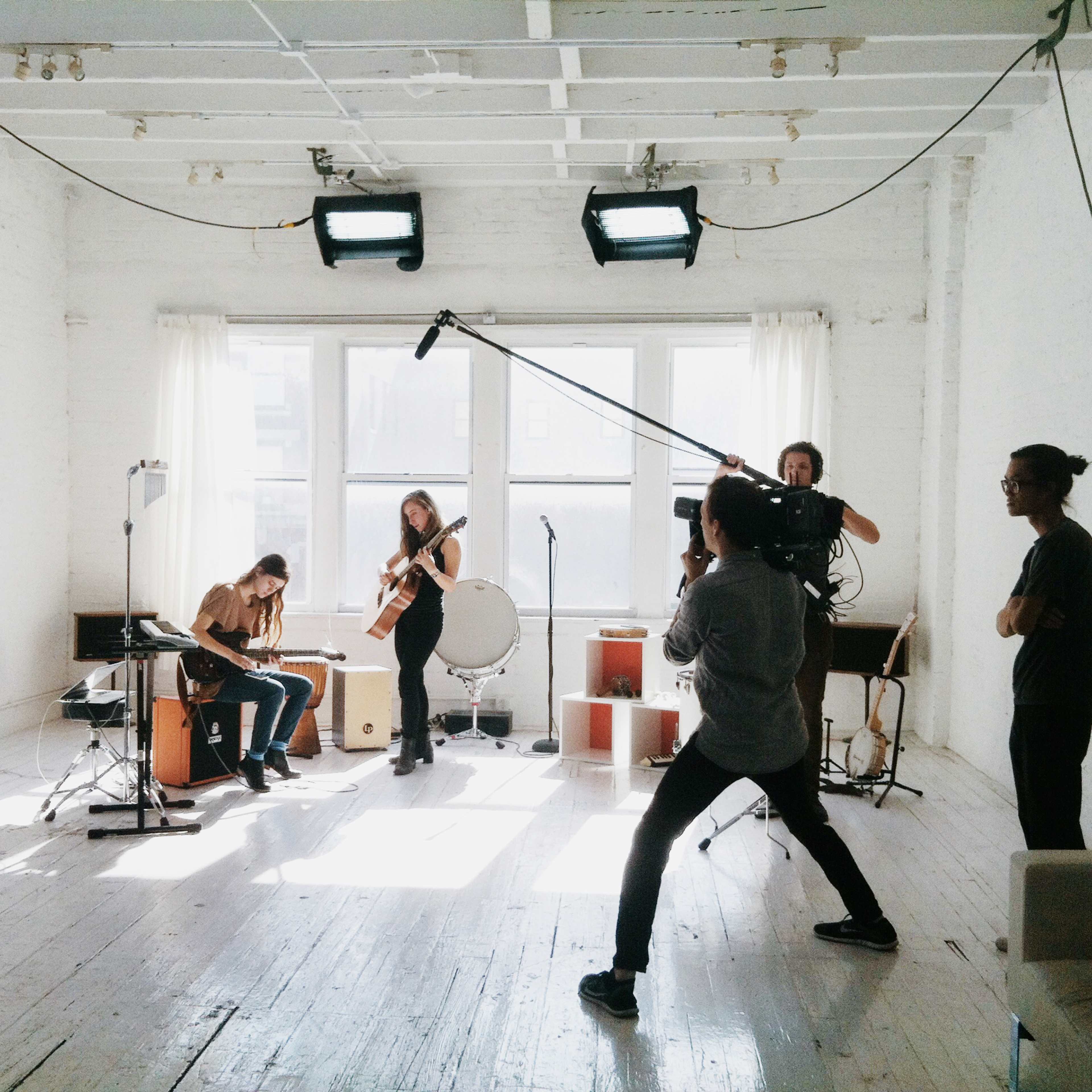 A group of musicians is performing in a well-lit studio while a videographer records the session.