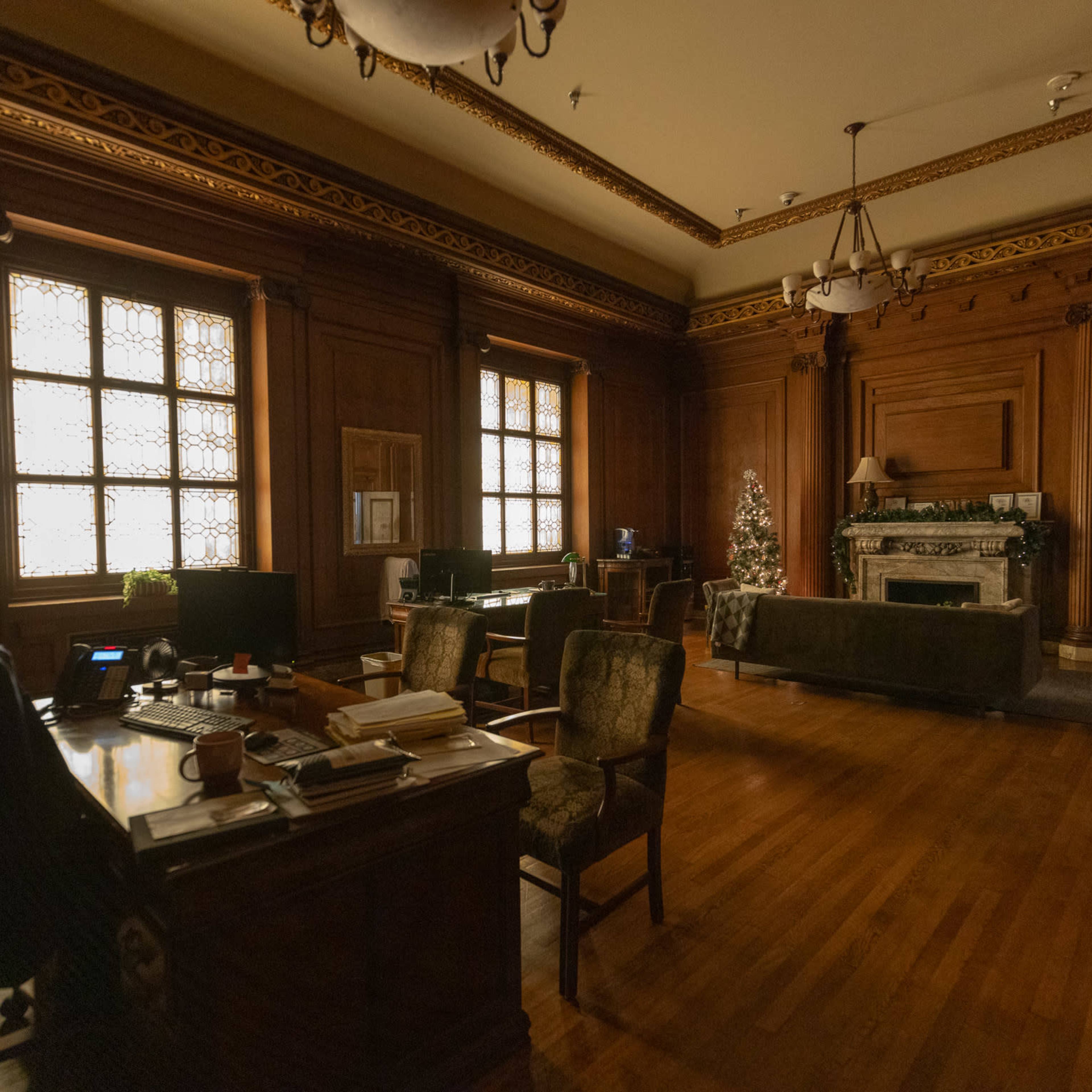 A spacious, wooden-paneled office featuring a desk, chairs, and a decorated Christmas tree in the corner.