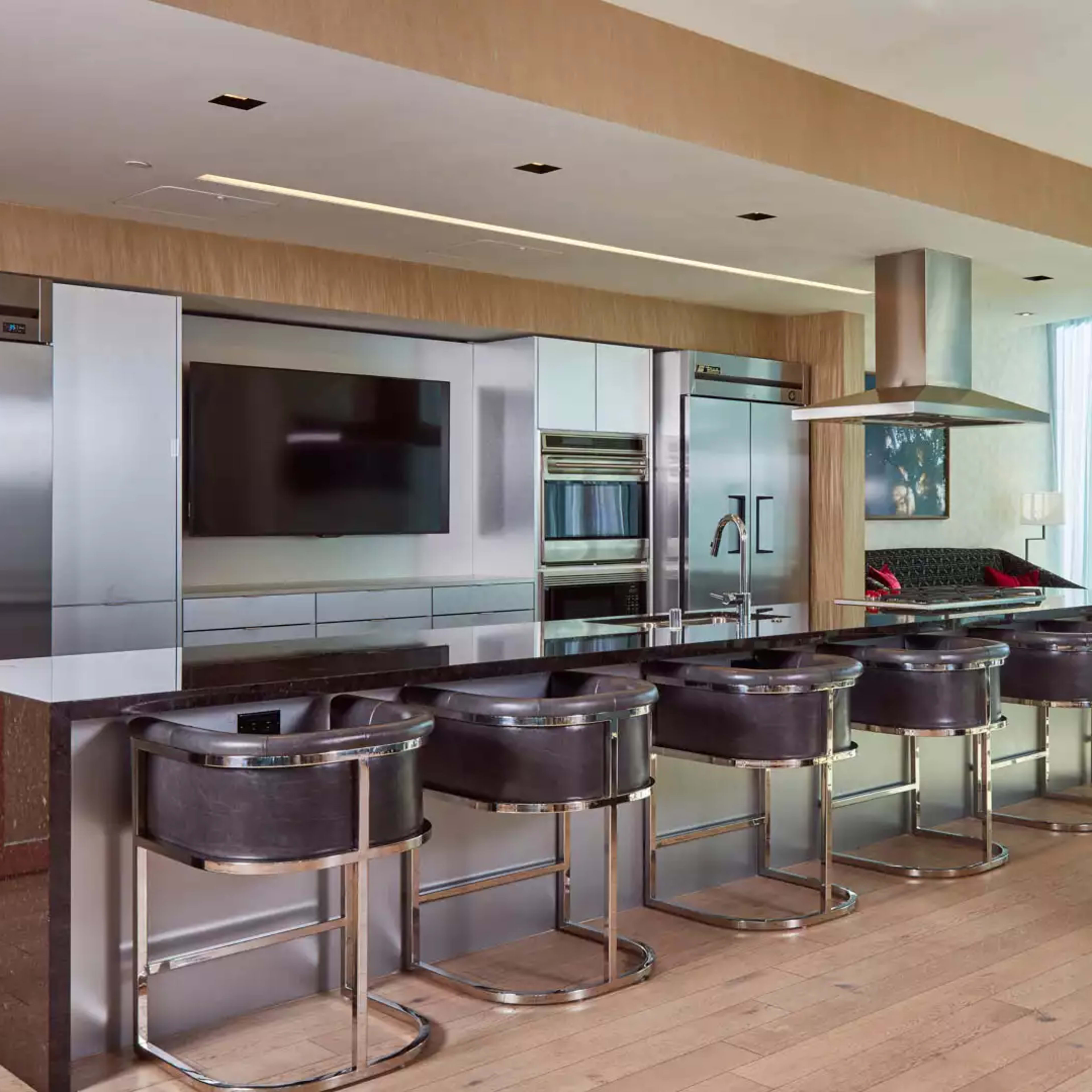 A modern kitchen with stainless steel appliances, a large island with six black bar stools, and a dining area with a round table.