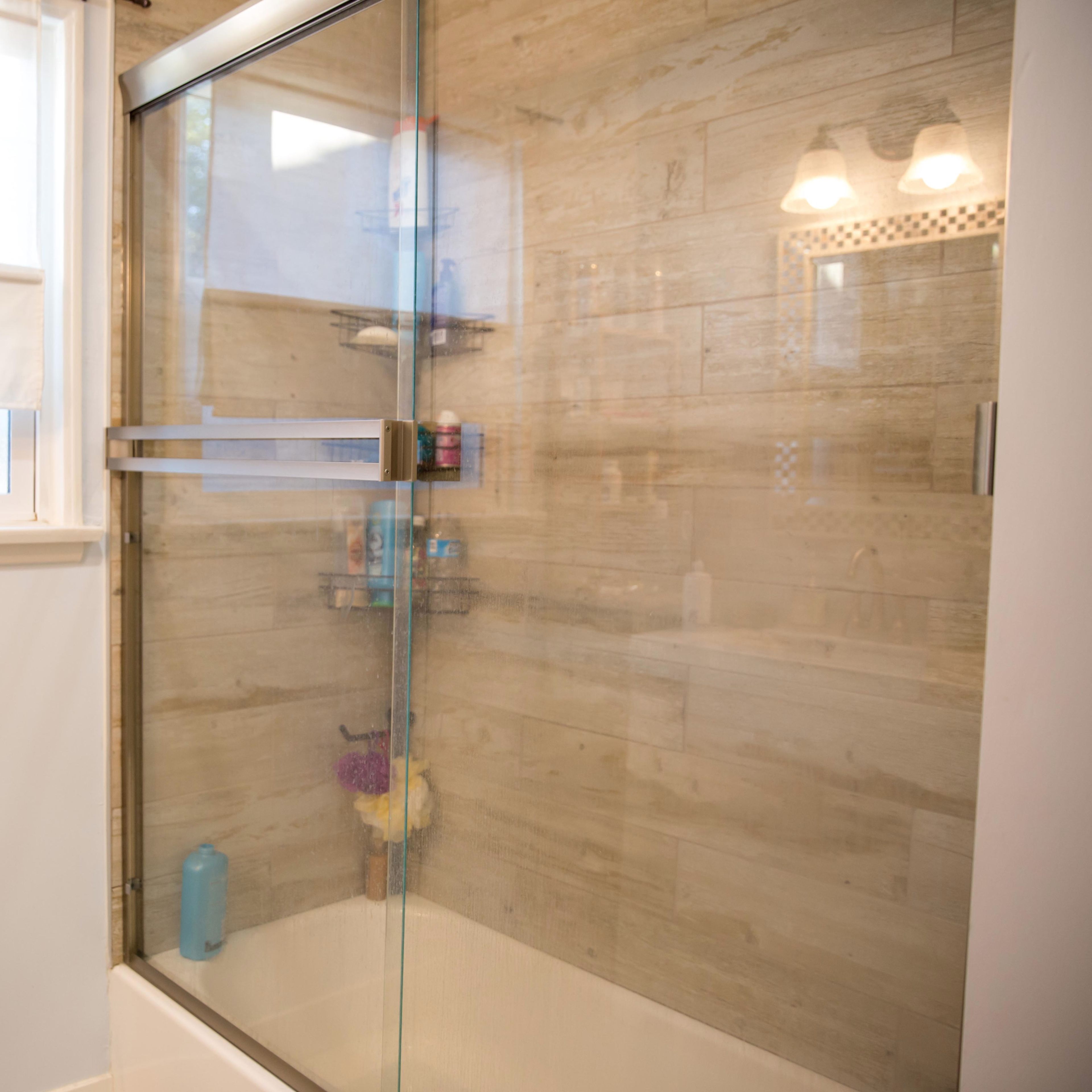 A glass shower enclosure with shelves containing various toiletries, set against a textured tile wall.