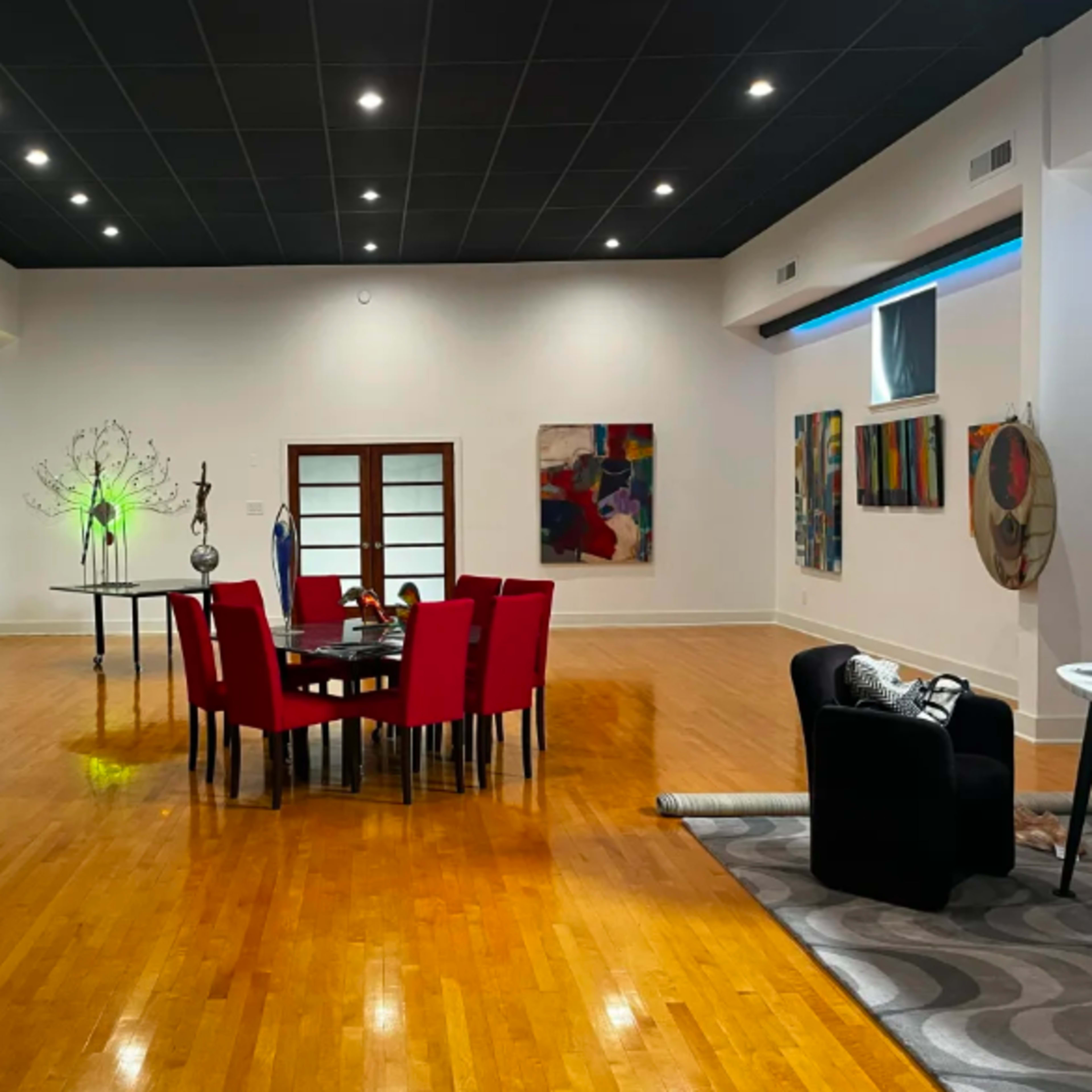 A spacious room features a round dining table surrounded by red chairs, with various artistic decorations and paintings on the walls.