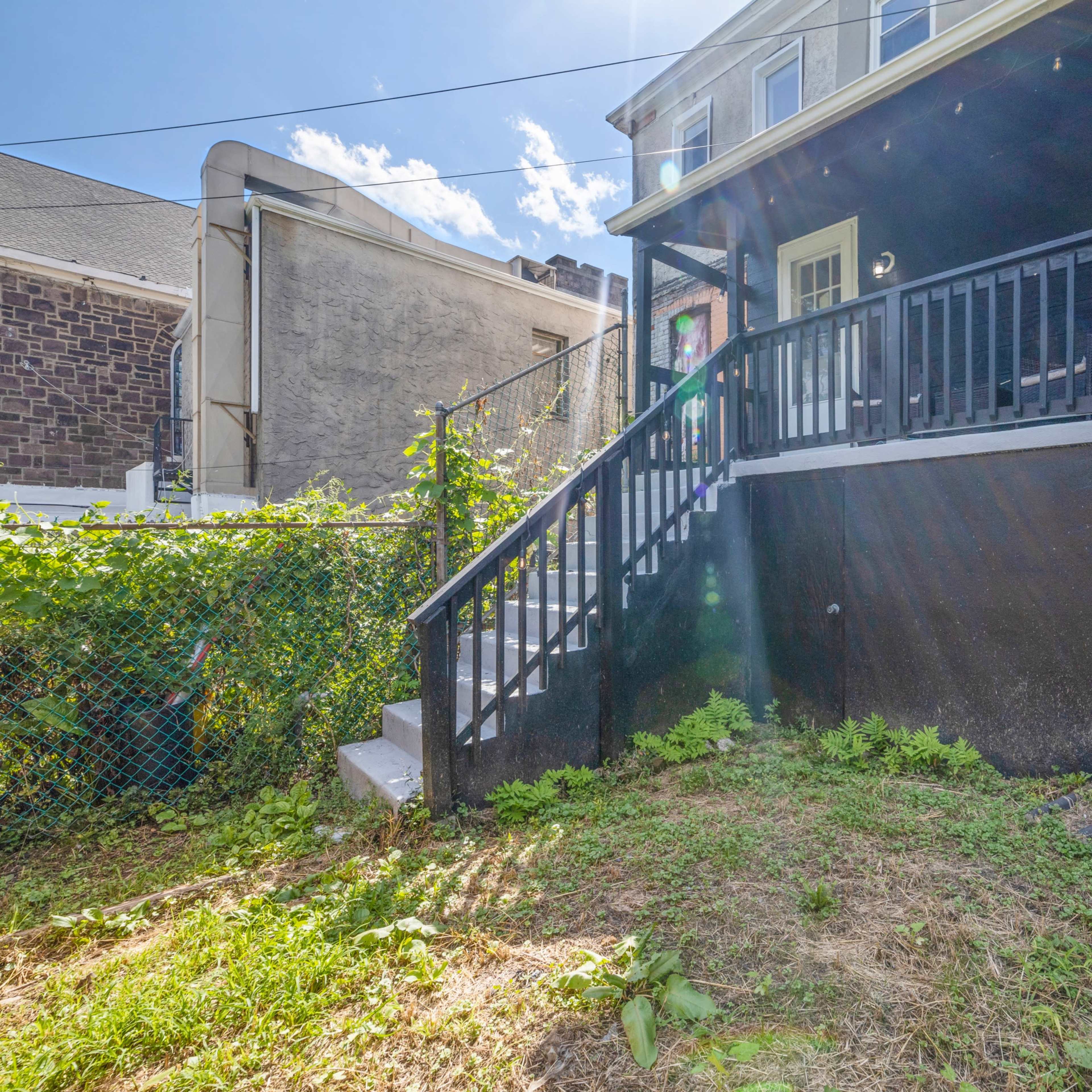A backyard with a set of stairs leading up to a porch, surrounded by overgrown grass and vegetation.