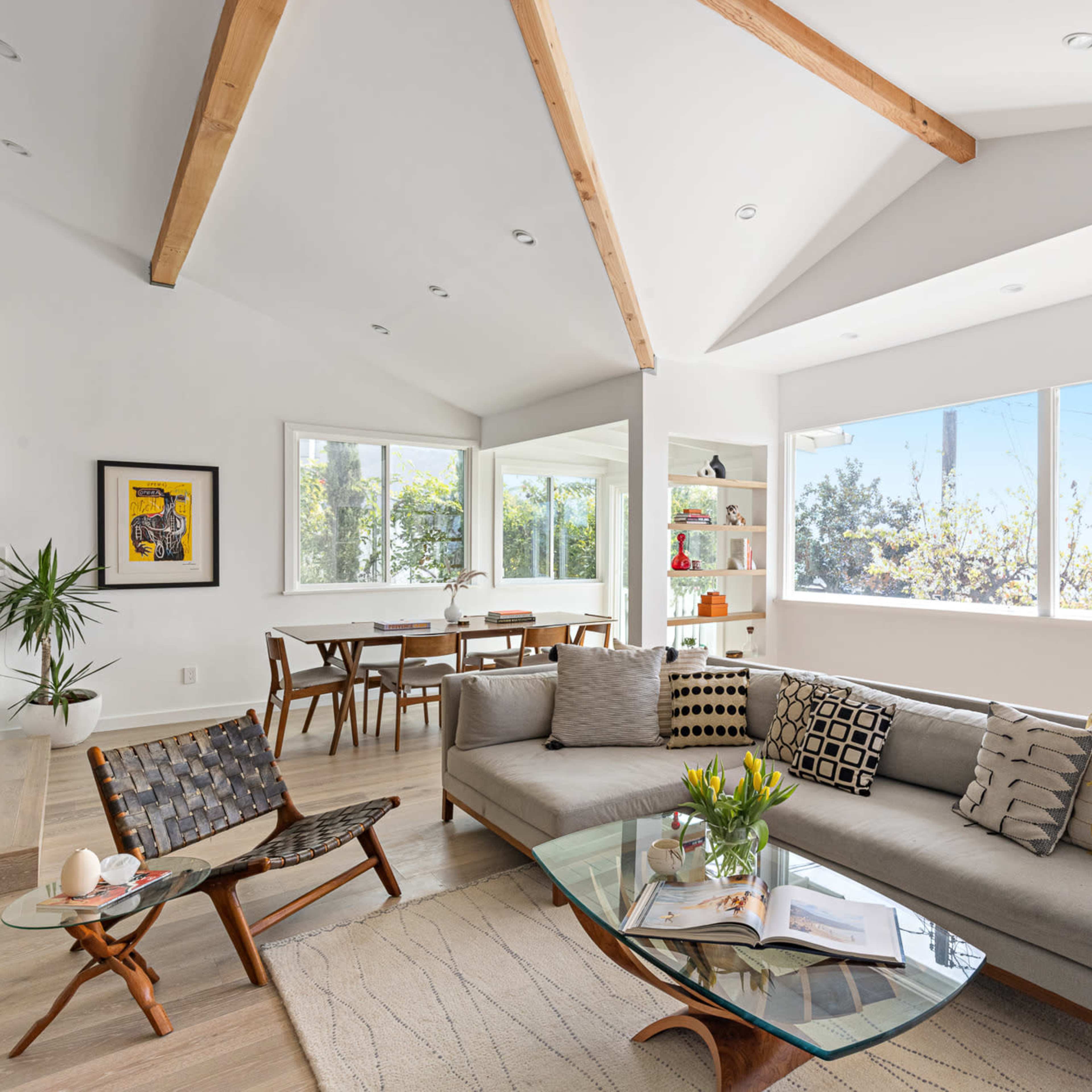 A modern living room with a sectional sofa, a glass coffee table, and large windows allowing natural light to fill the space.