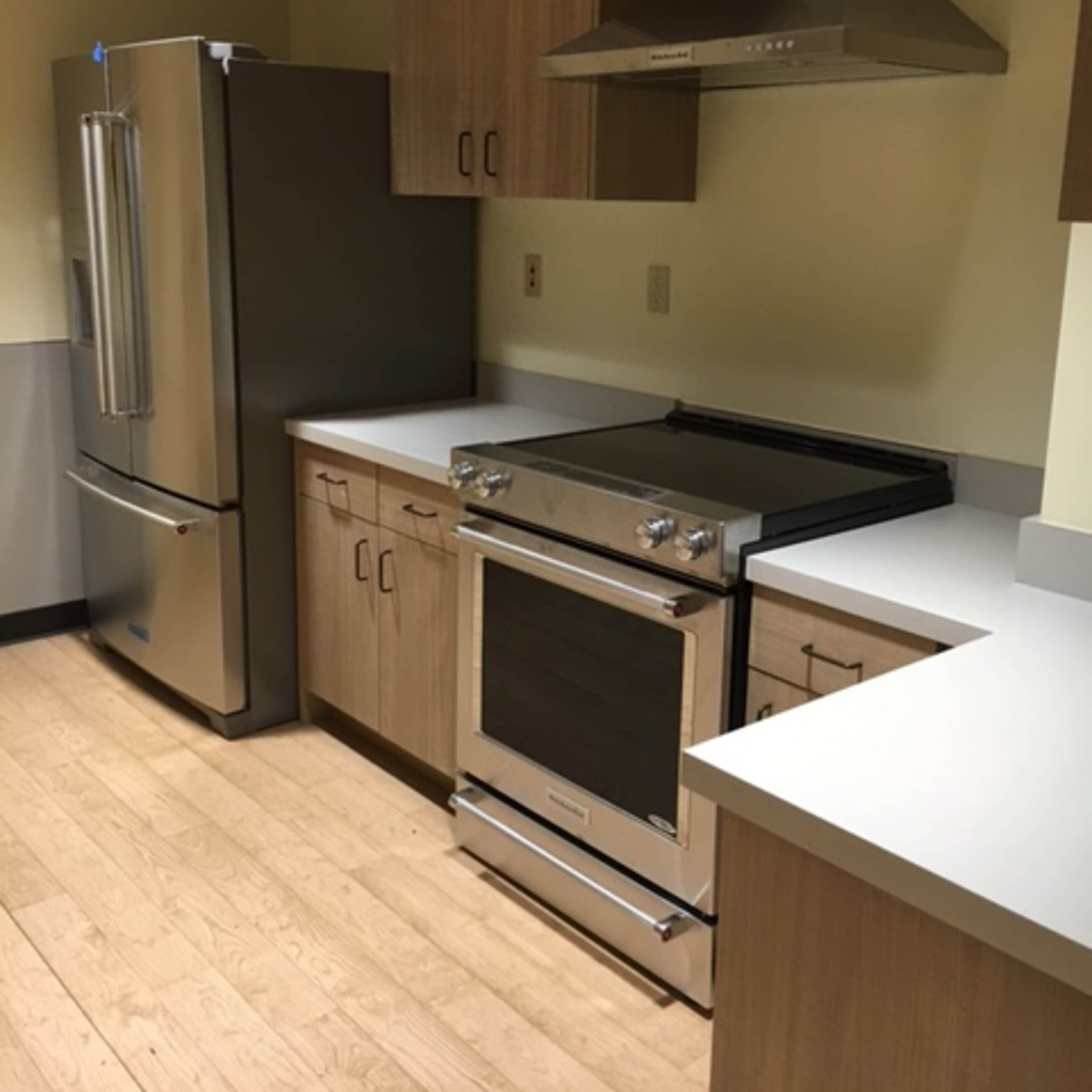A modern kitchen with light wood cabinetry, a stainless steel refrigerator, an oven range, and a hood above it.