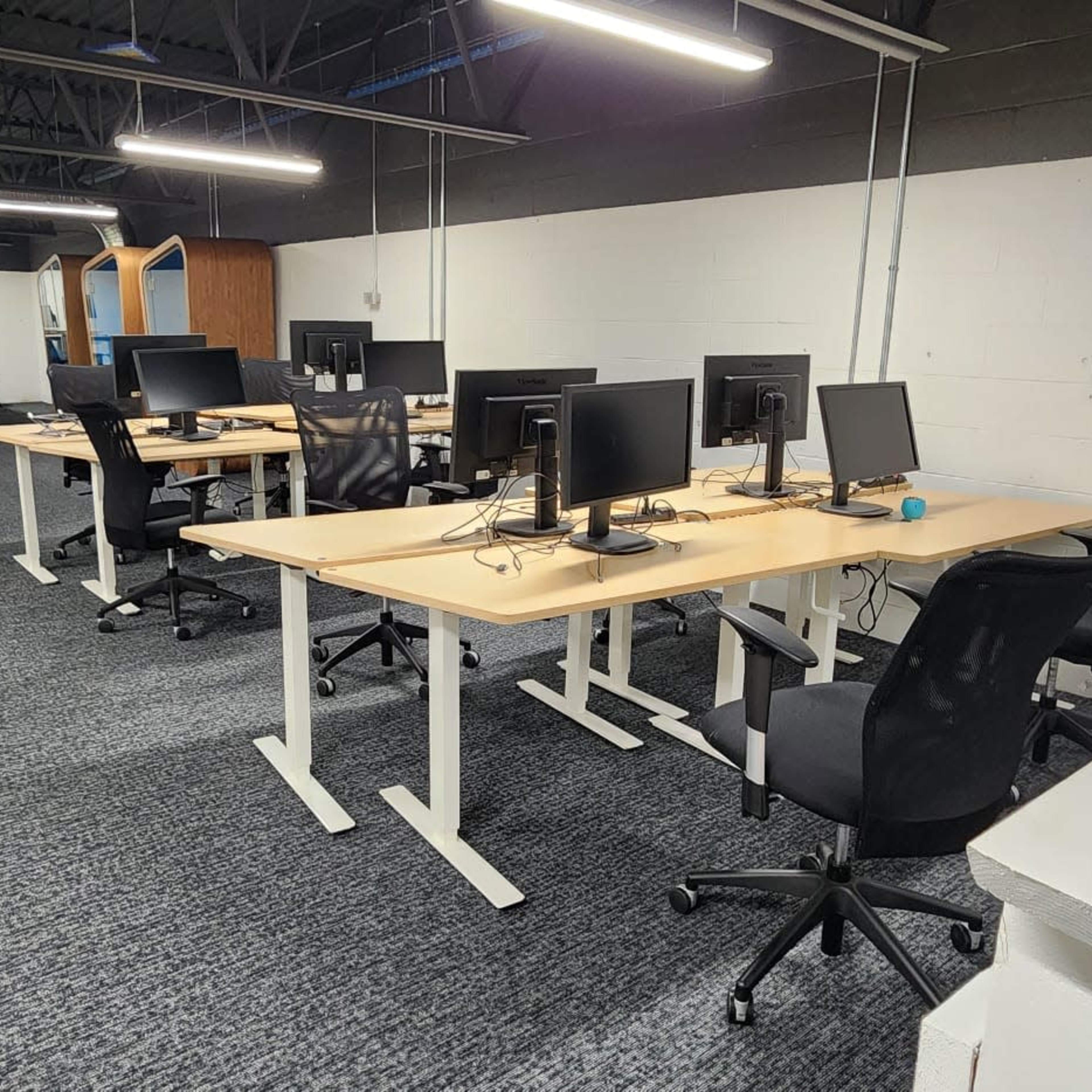 A row of empty desks with computers in an office space featuring gray carpeting and white walls.