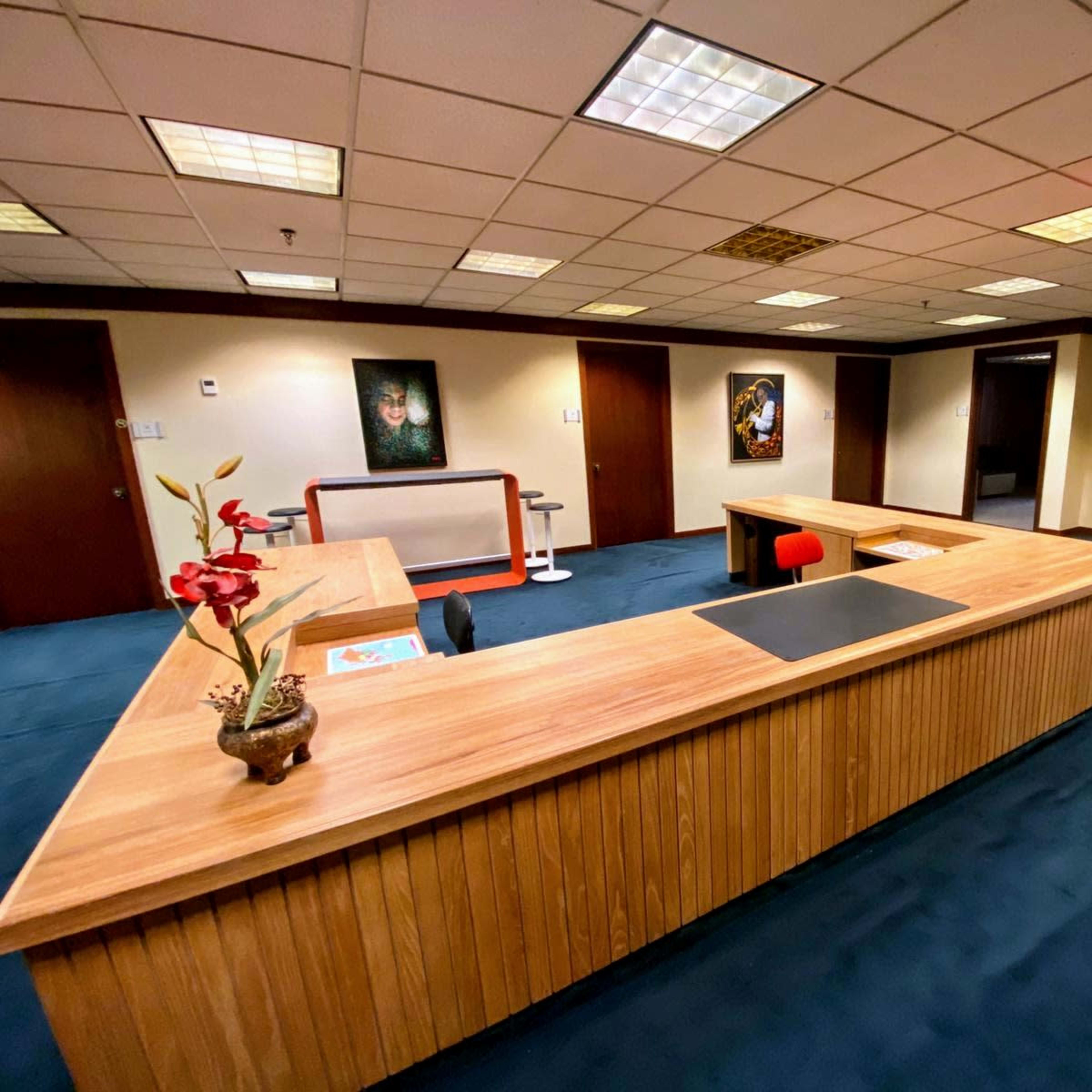 An office space with a wooden reception desk, blue carpet, and several framed artworks on the walls.