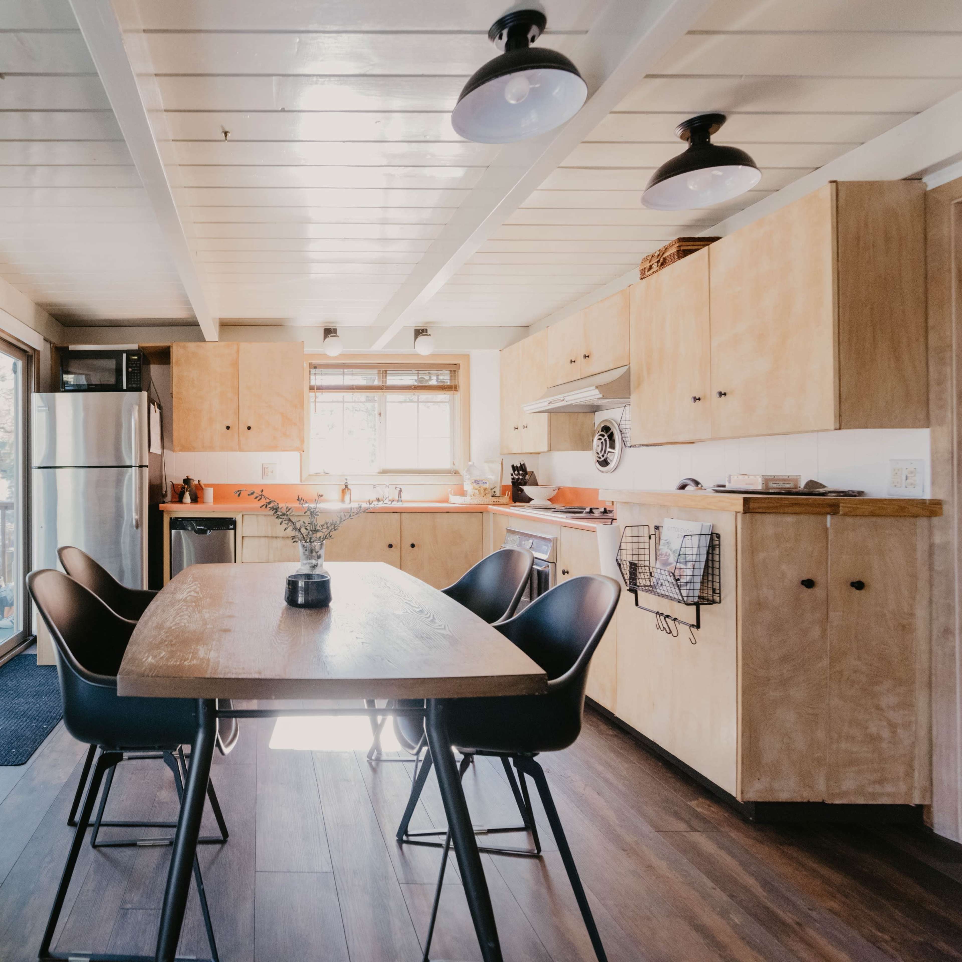 A modern kitchen features a wooden table surrounded by black chairs, with stainless steel appliances and sliding doors leading to an outdoor area.