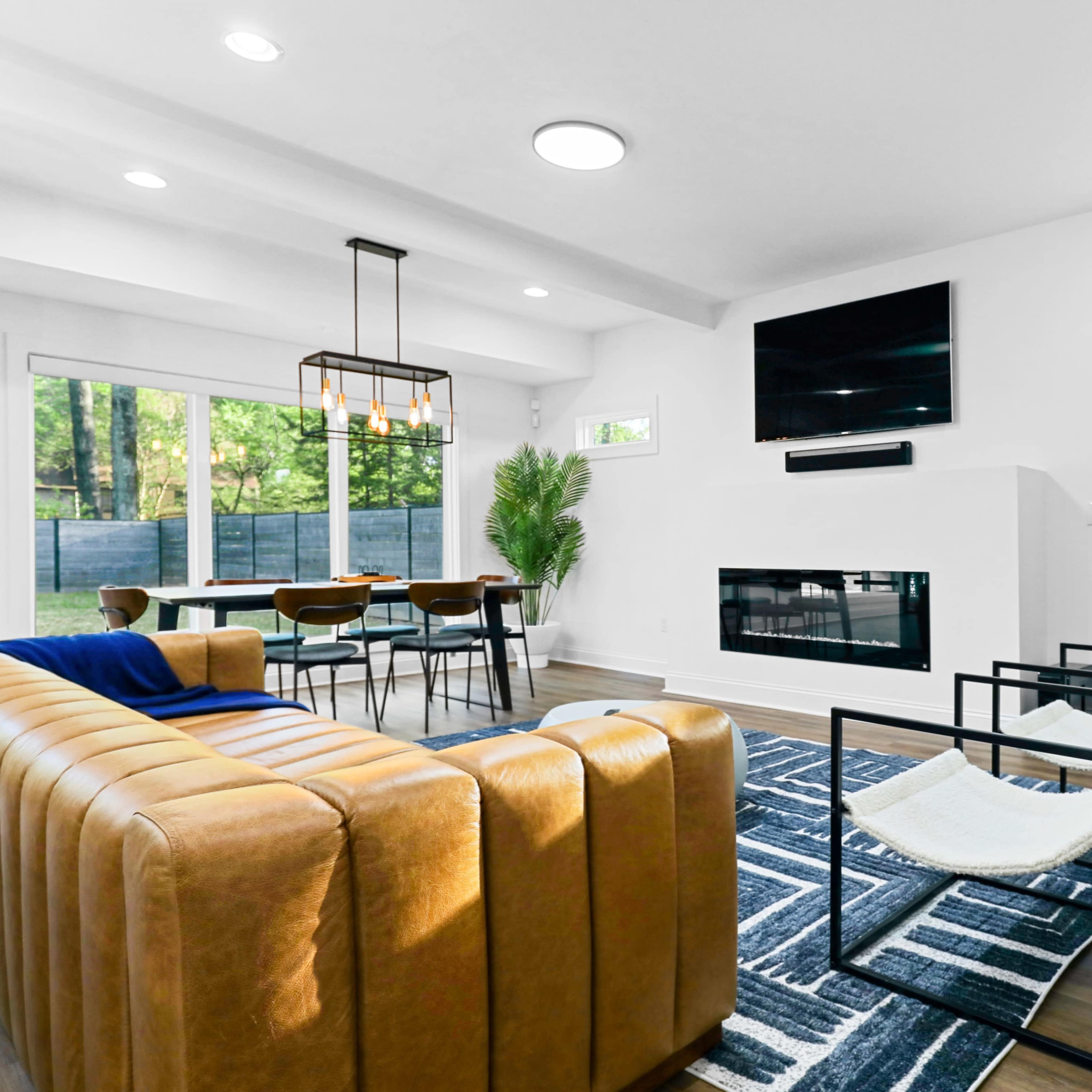 A modern living room with a brown leather sofa, a black television mounted on the wall, and a dining area featuring a wooden table and chairs.