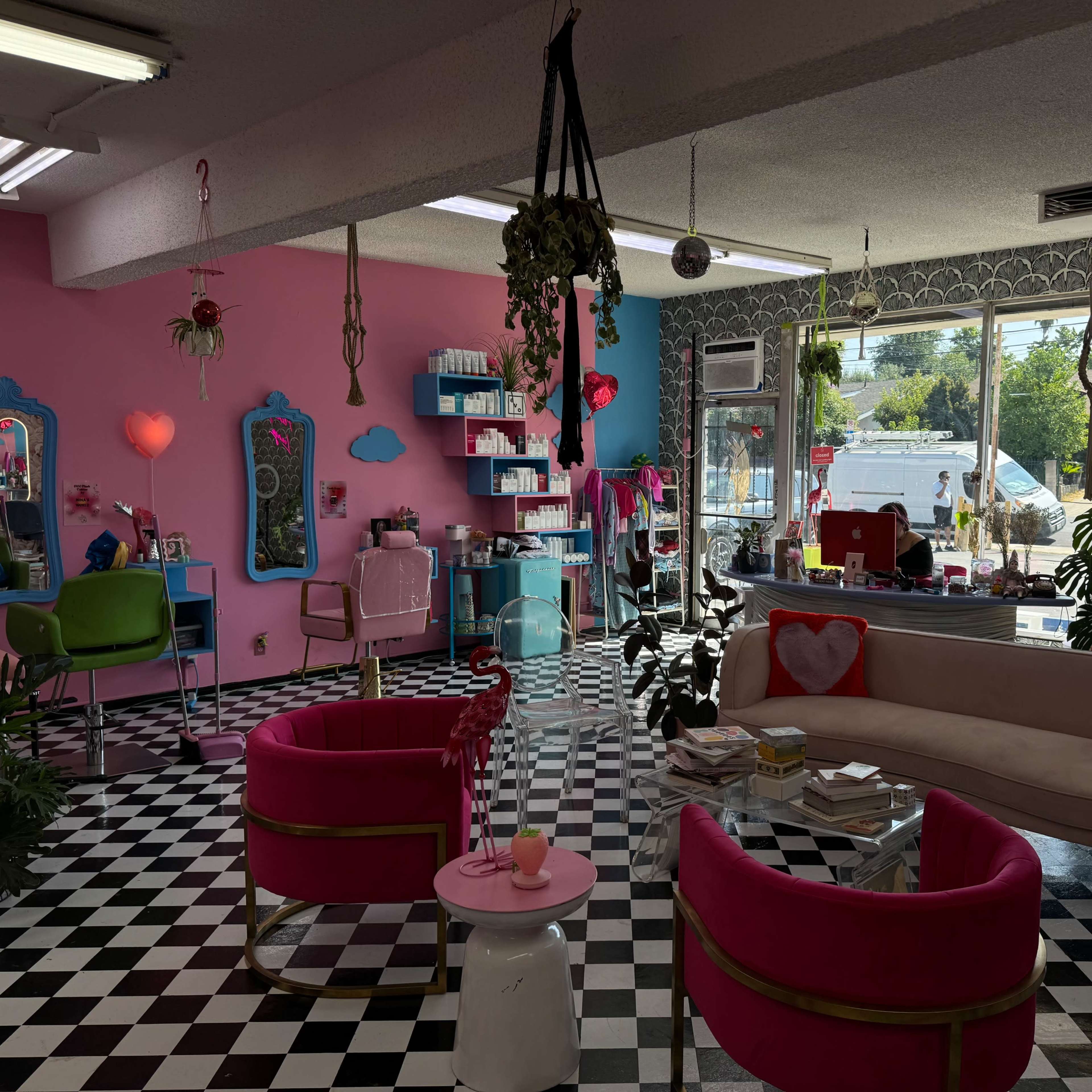 A brightly colored beauty salon with a checkered floor, pink and green furniture, and various plants scattered throughout the space.