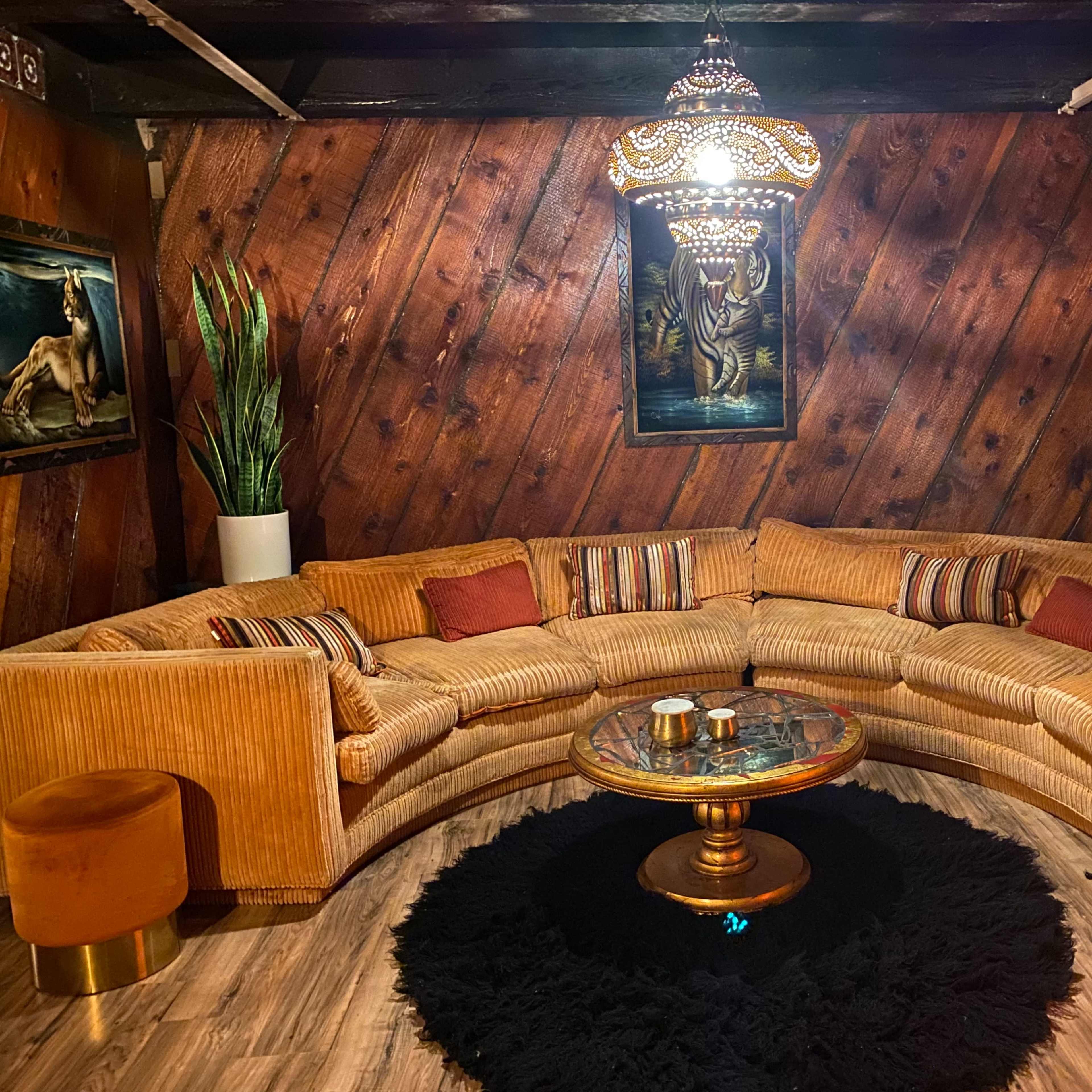 A spacious, circular sectional sofa is arranged around a glass coffee table on a black area rug, with potted plants and animal-themed artwork on the walls.