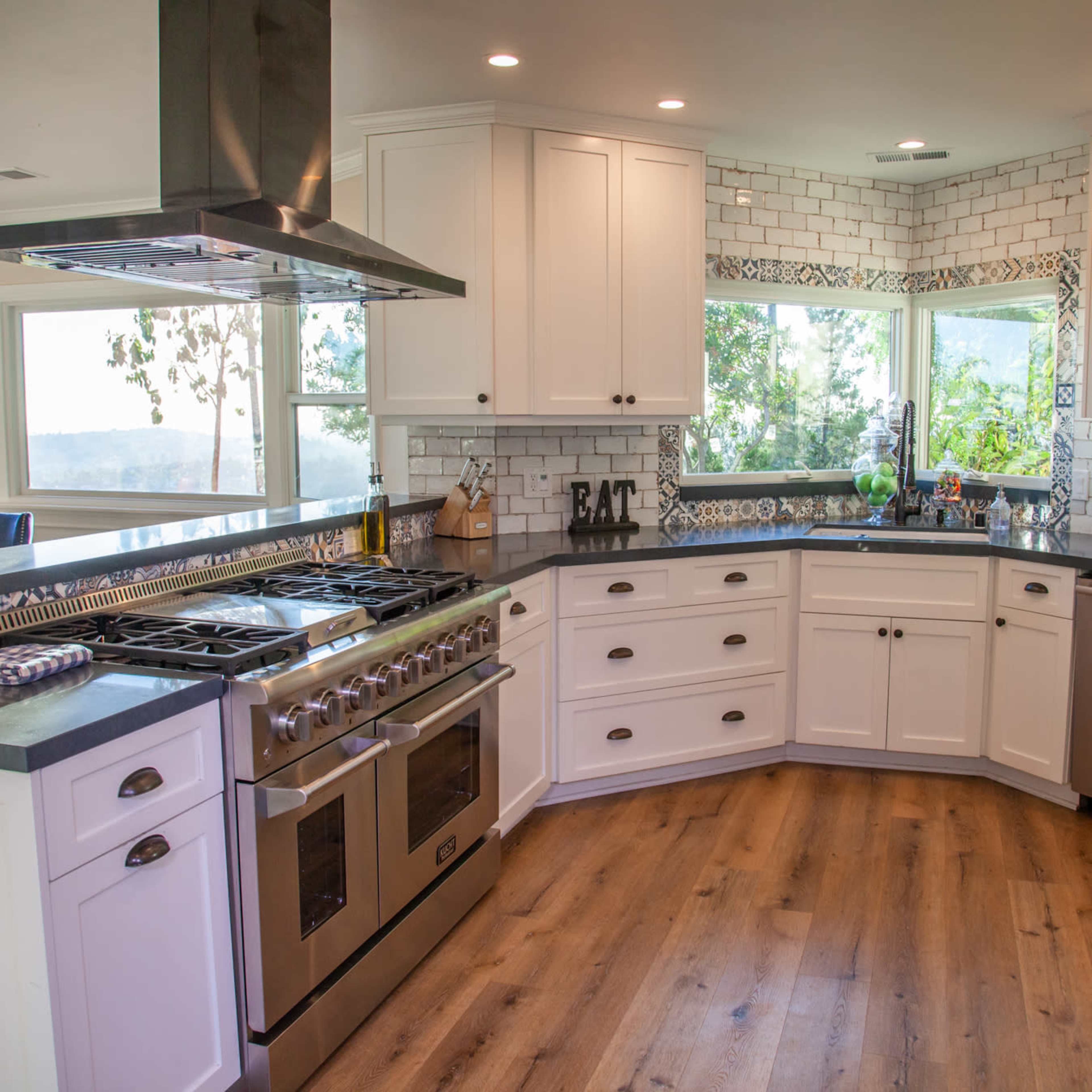 A modern kitchen features white cabinetry, stainless steel appliances, and a spacious countertop with large windows overlooking a scenic view.