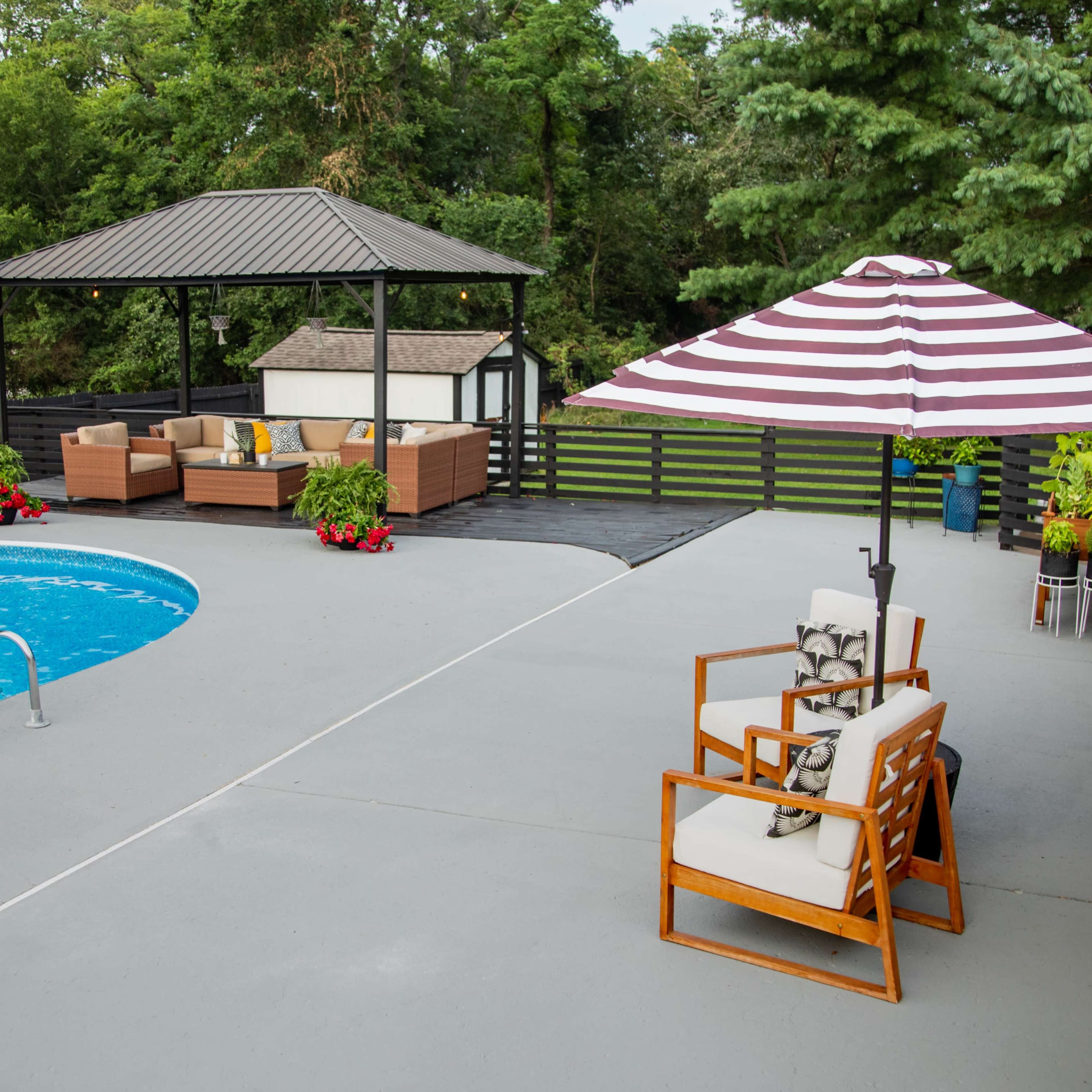 A spacious backyard features a swimming pool, a shaded seating area under a gazebo, and a striped umbrella beside a lounge chair.