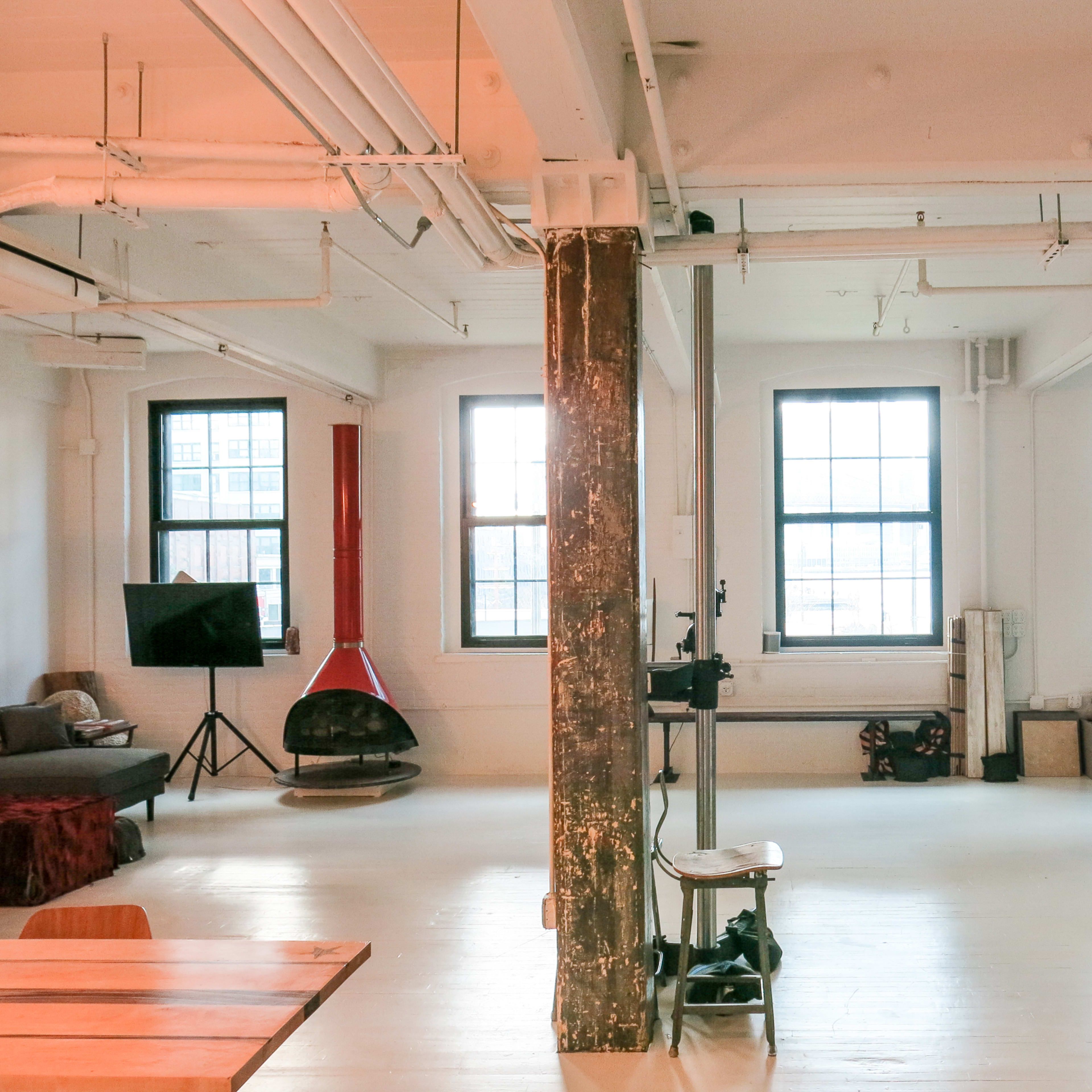 A spacious studio with large windows, wooden beams, and various furniture and equipment arranged throughout the room.
