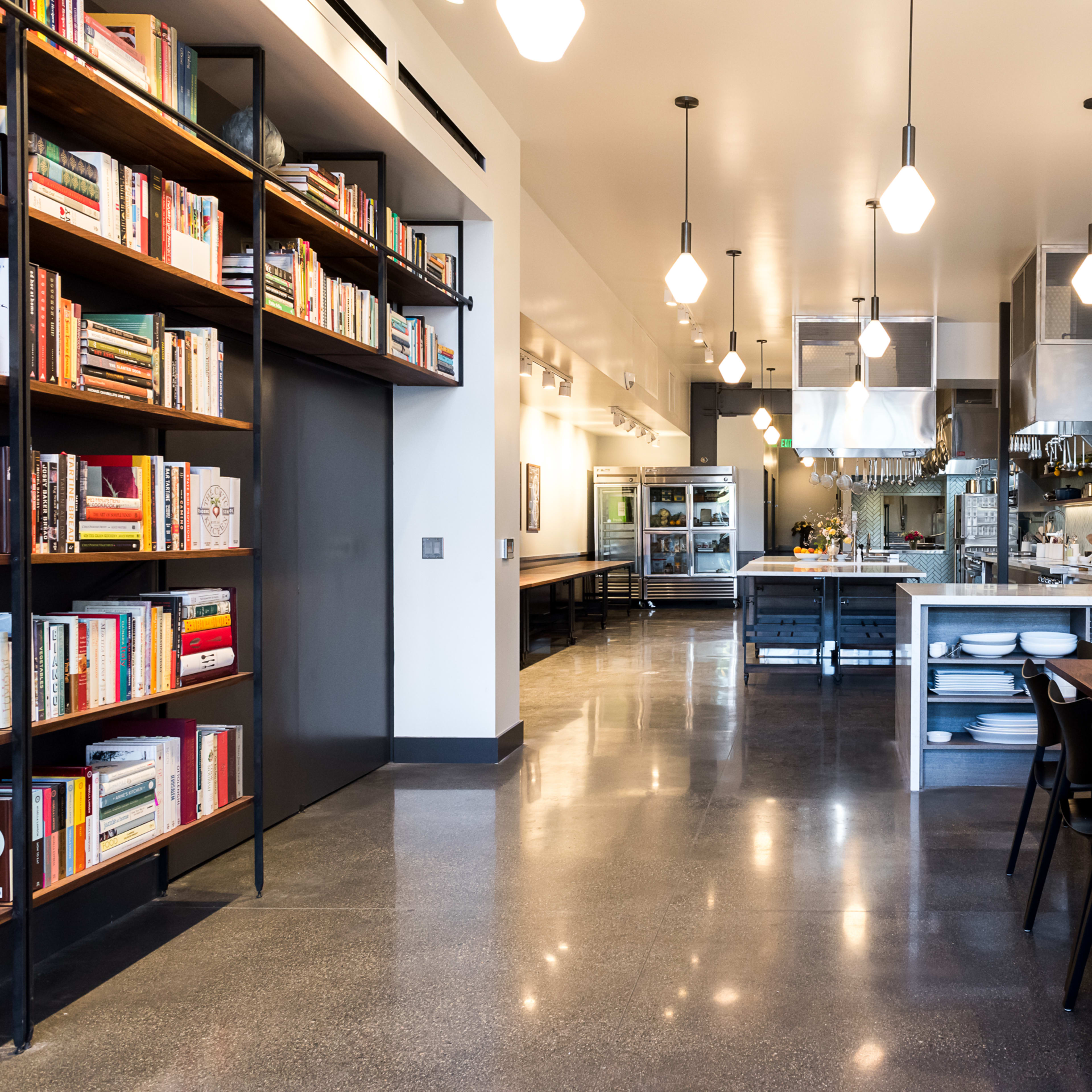A modern kitchen and dining area with a long wooden table, shelves filled with books, and stainless steel appliances.