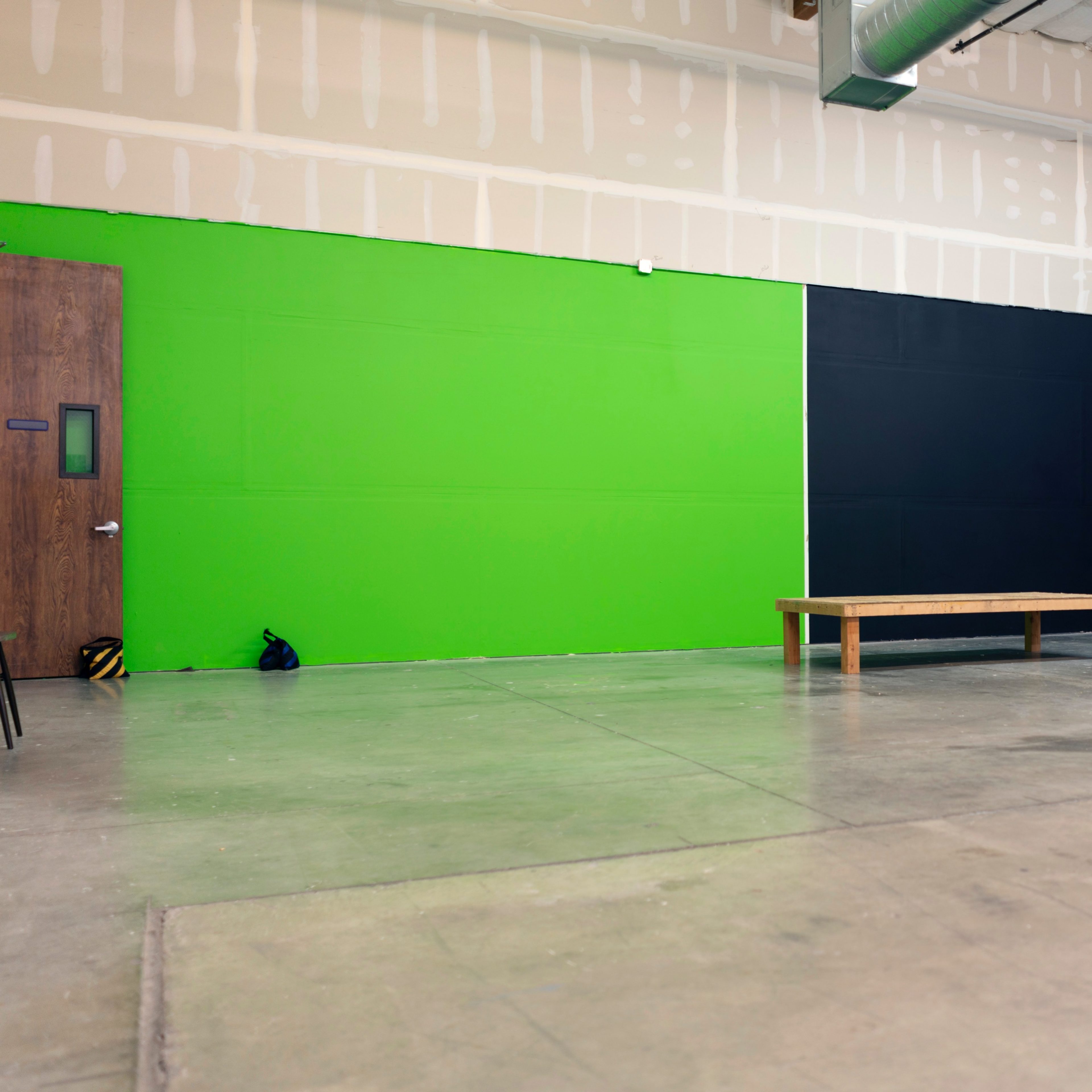 A spacious interior with a green wall, a black wall, a wooden table in the center, and a concrete floor.