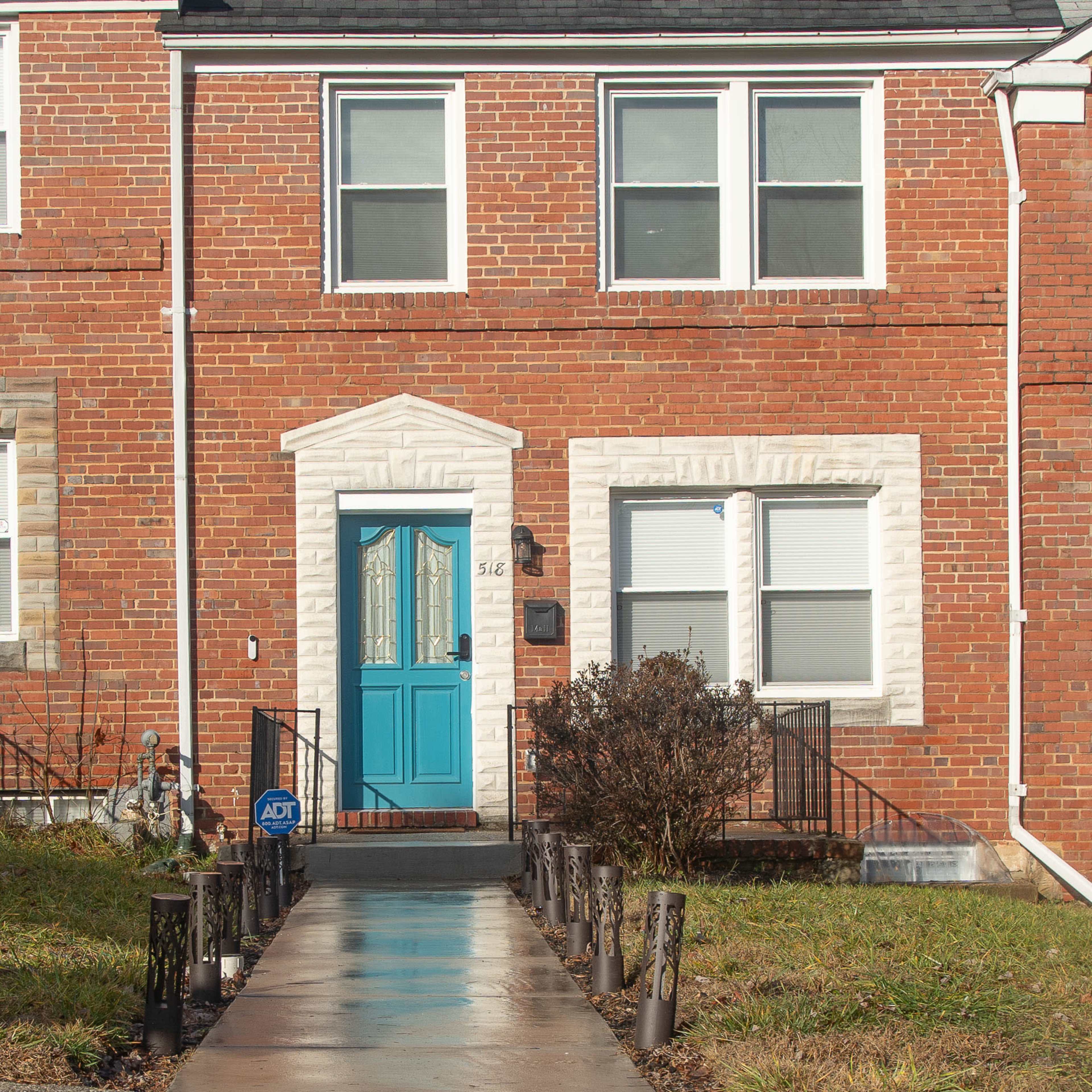 A two-story brick townhouse with a blue front door and a walkway leading to it.