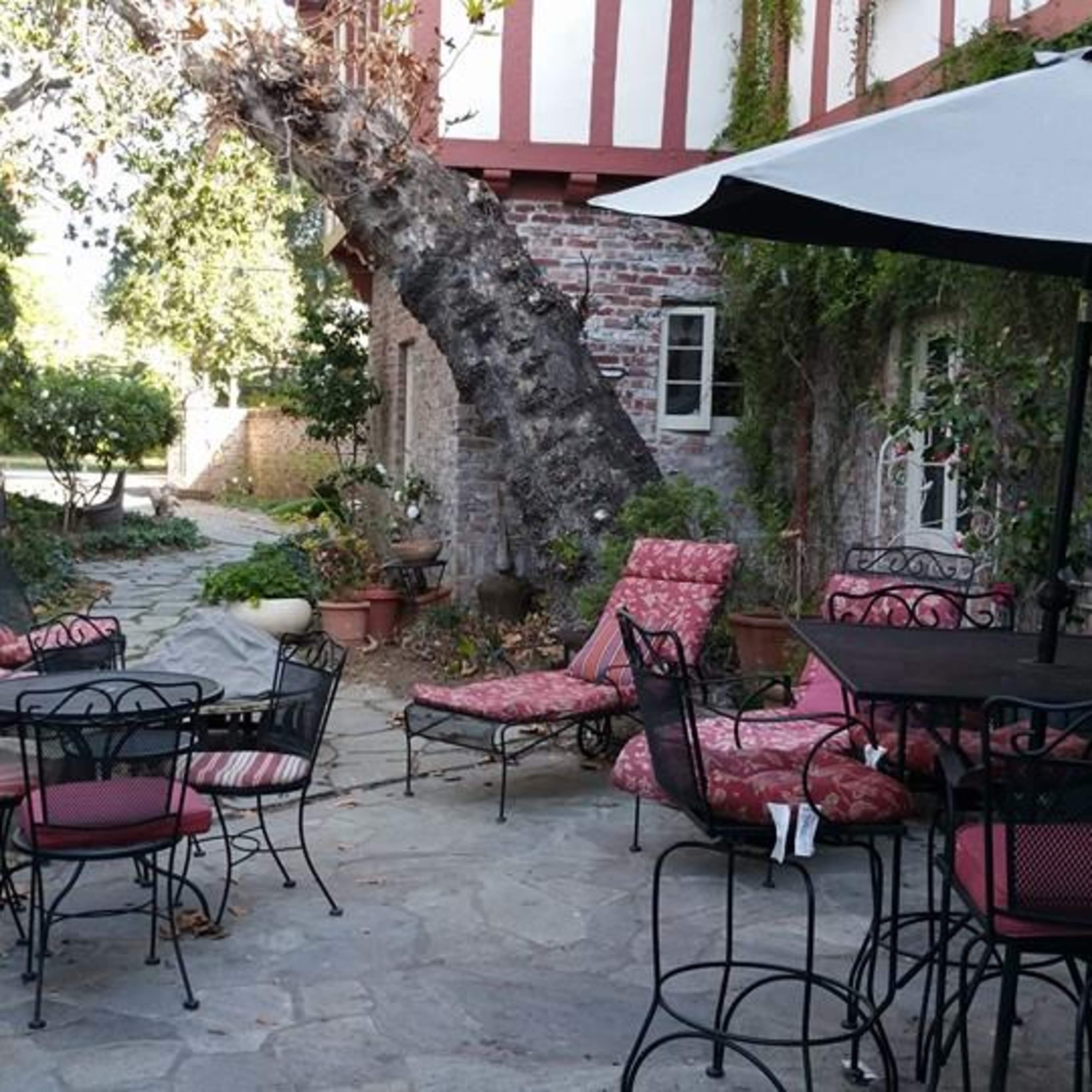 A stone patio with wrought iron furniture and a large tree surrounded by greenery and a brick wall.