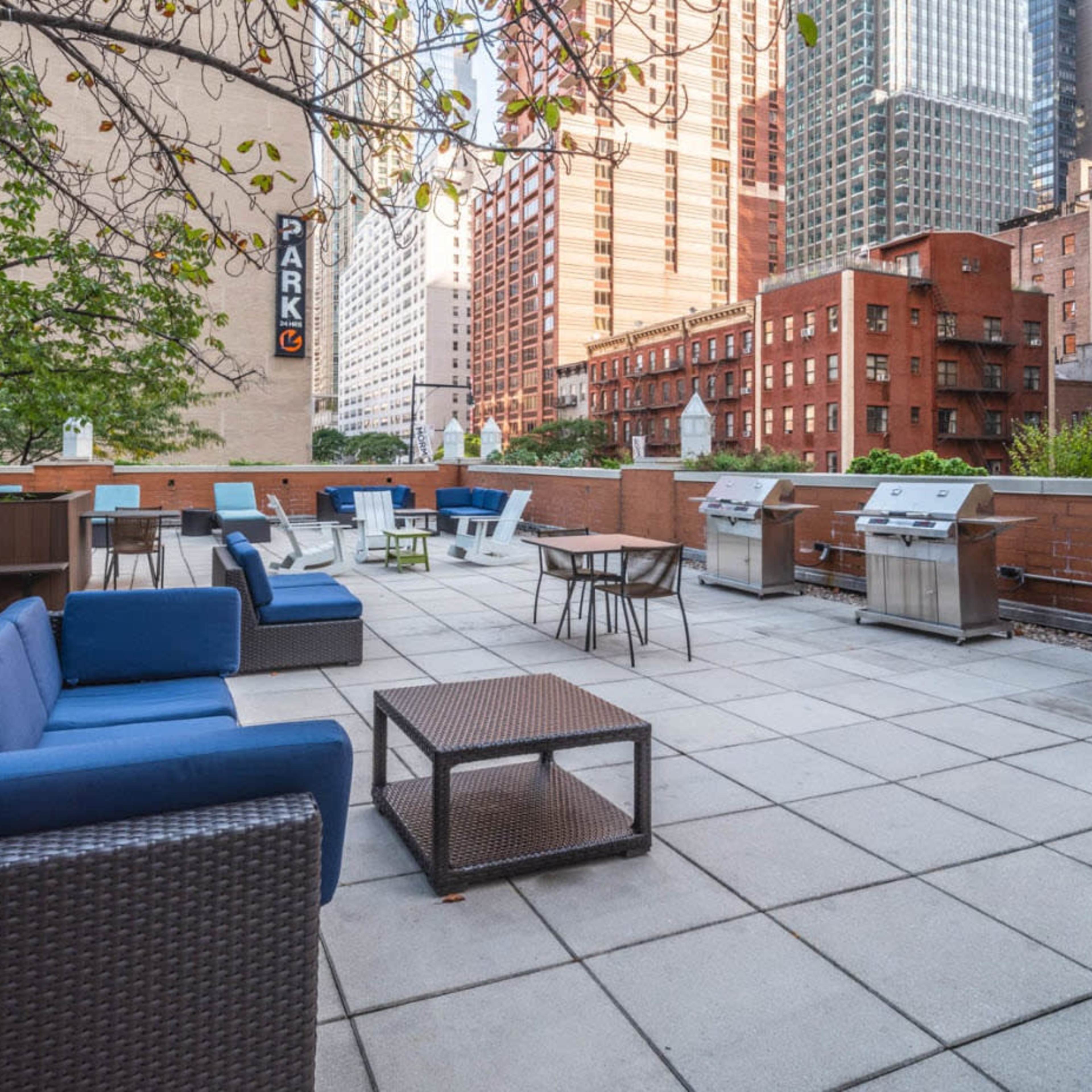 The rooftop terrace features outdoor seating and several barbecue grills surrounded by city buildings.